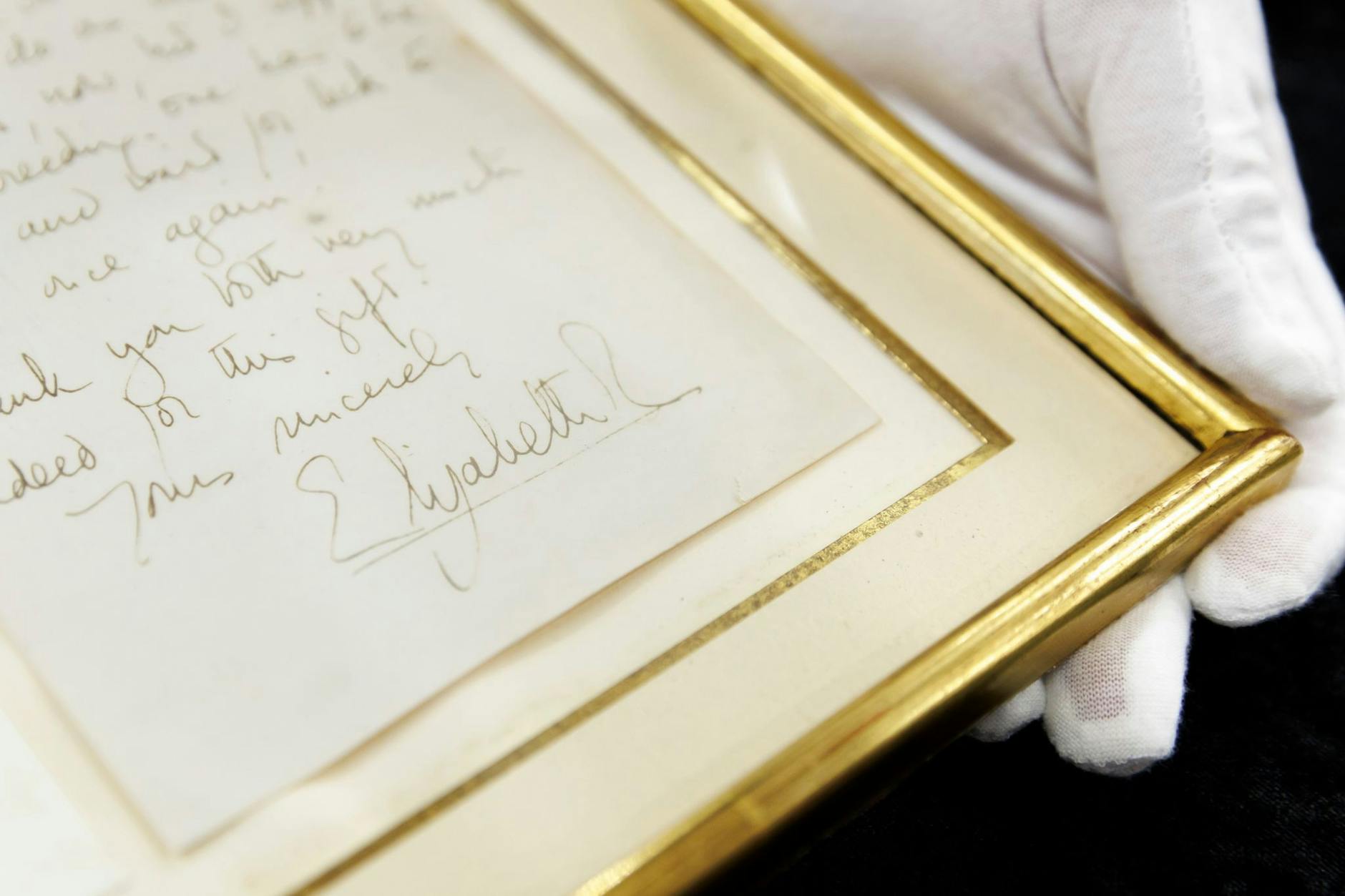 PRODUKTION - Ein Brief von Königin Elizabeth II. ist für 8300 Euro versteigert worden. Die Unterschrift der Queen ist auf einer Kopie der Rückseite zu sehen, welche dem eingerahmten Brief beiliegt.