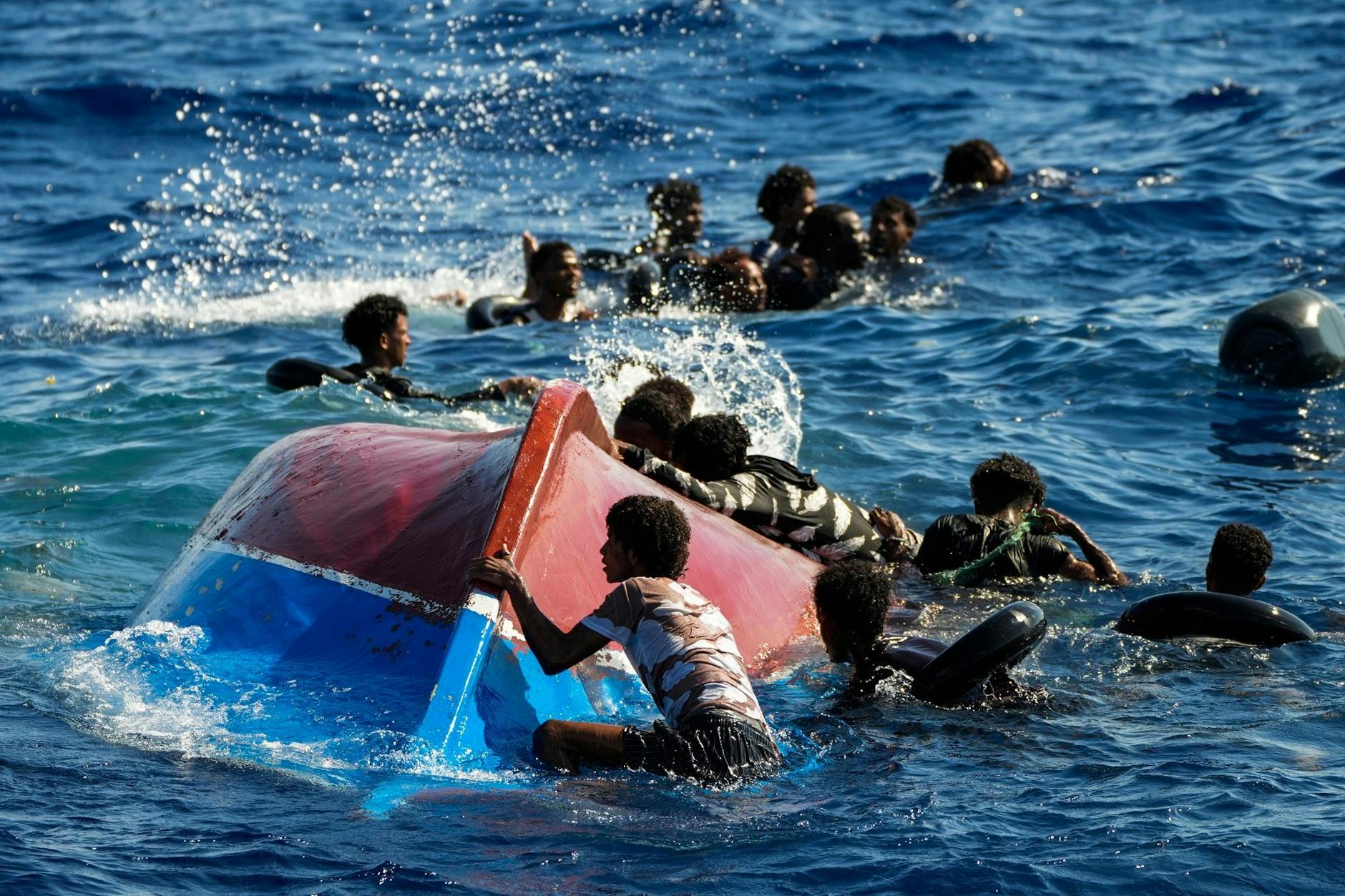 Migranten schwimmen neben ihrem umgestürzten Holzboot im Mittelmeer.