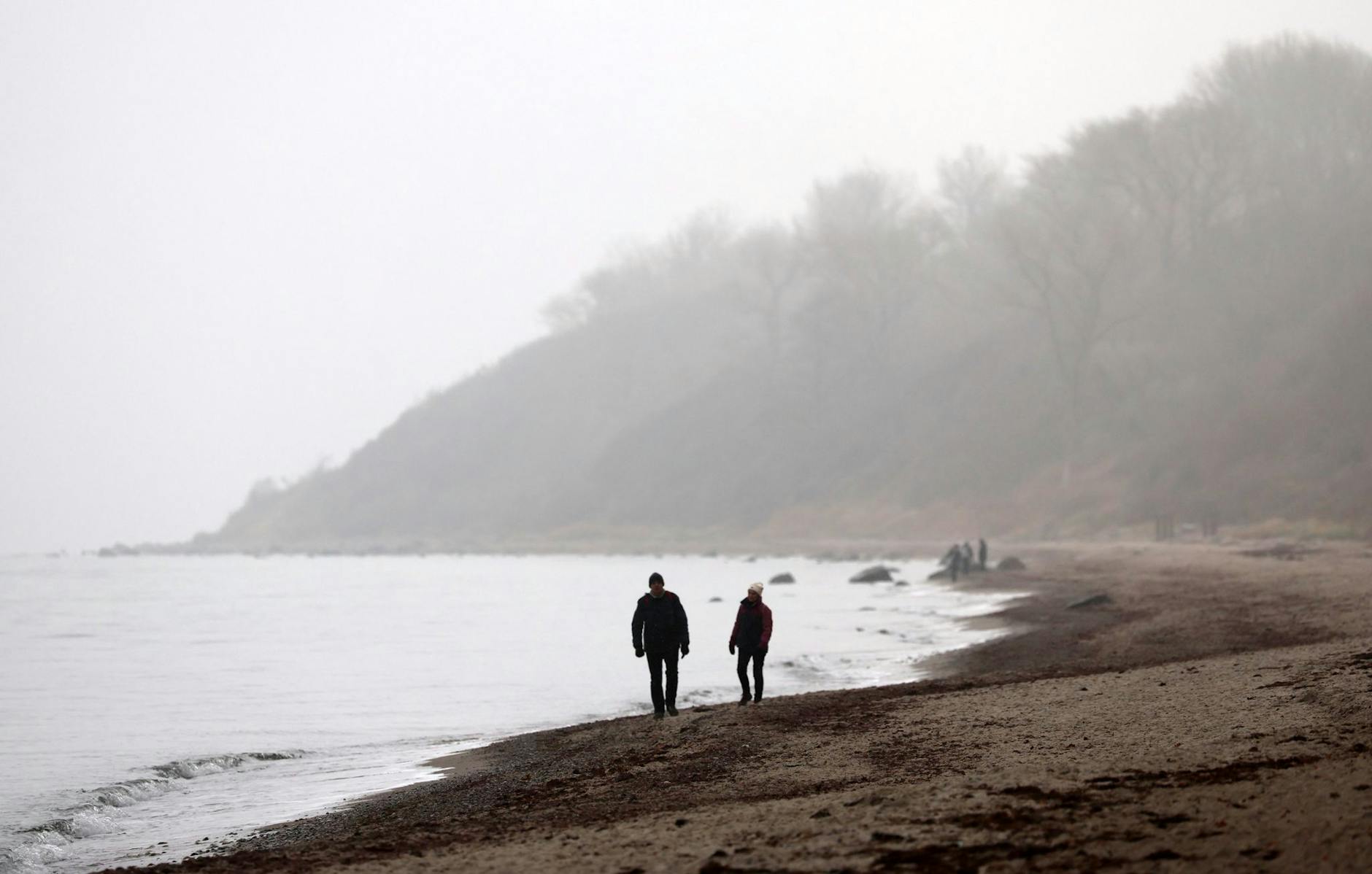 Zwei Spaziergänger sind bei grau-trübem Winterwetter an der Ostsee bei Rerik unterwegs.