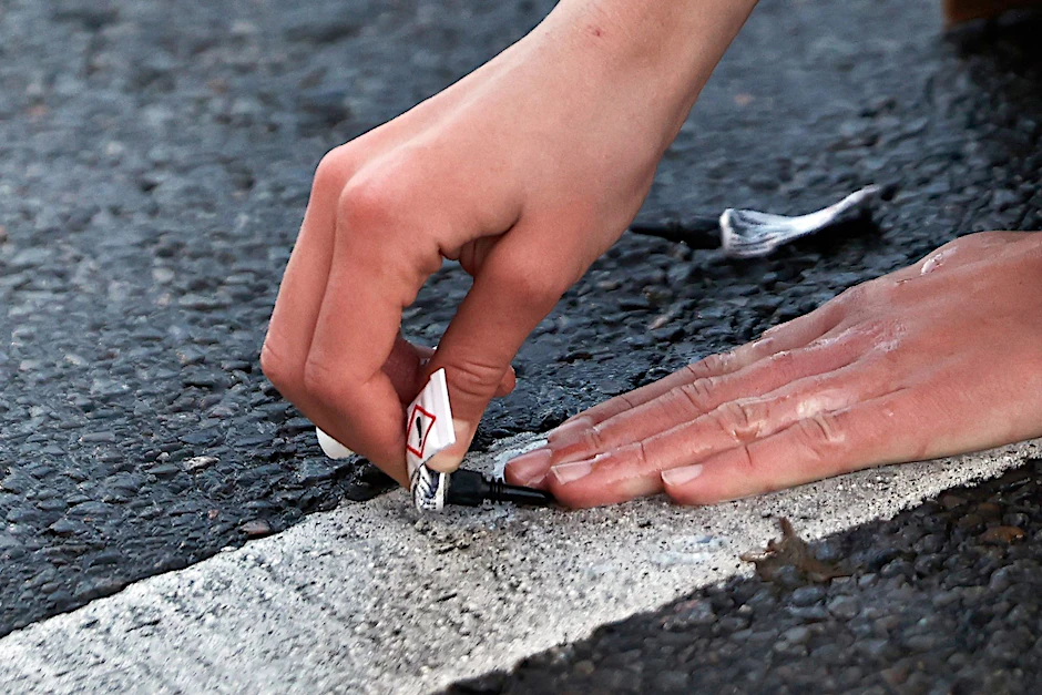 Ein Demonstrant klebt seine Hand in Berlin mit Sekundenkleber auf der Straße fest.  