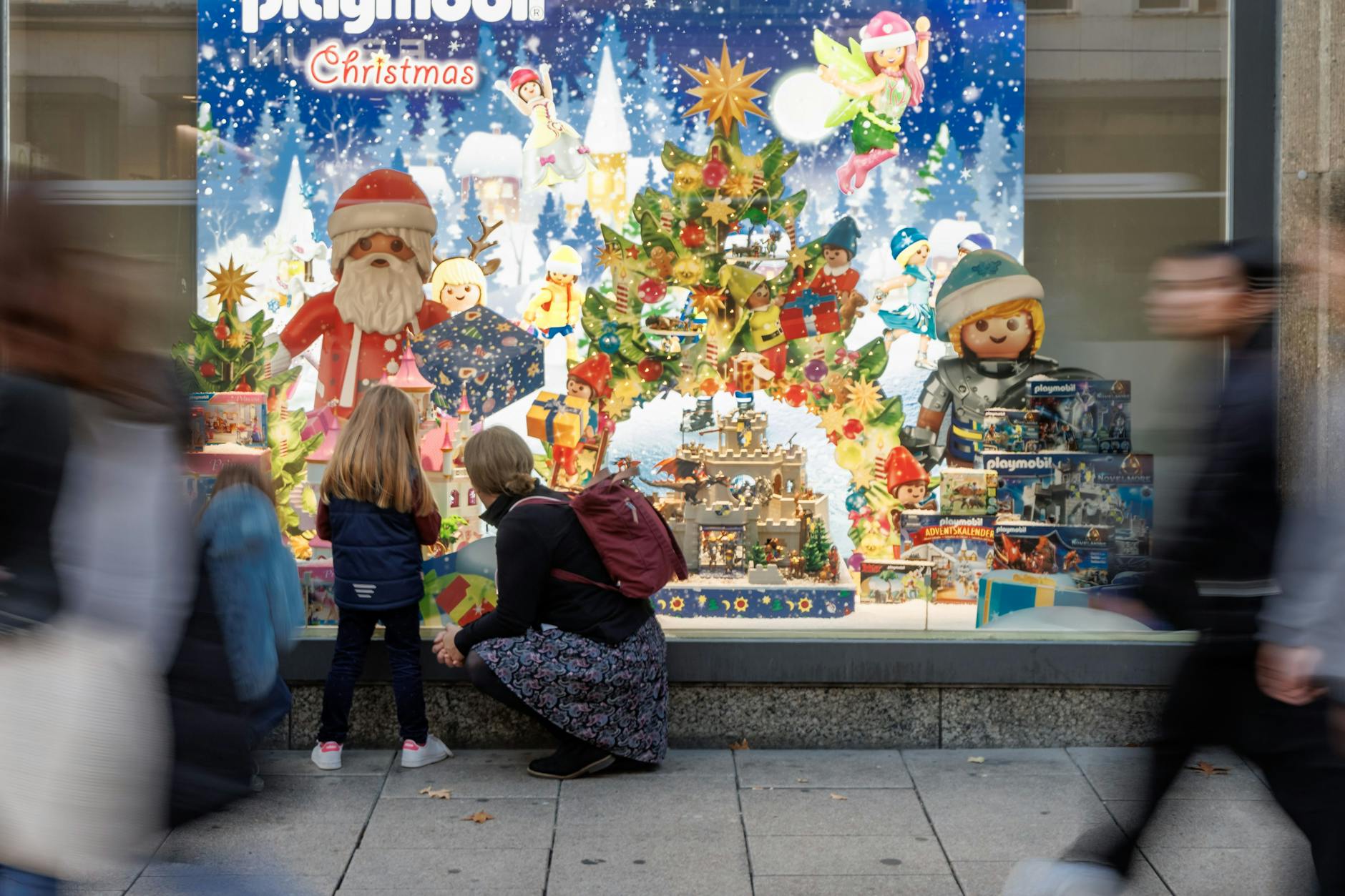 Eine Mutter und ihre Tochter betrachten ein weihnachtlich geschmücktes Schaufenster. 