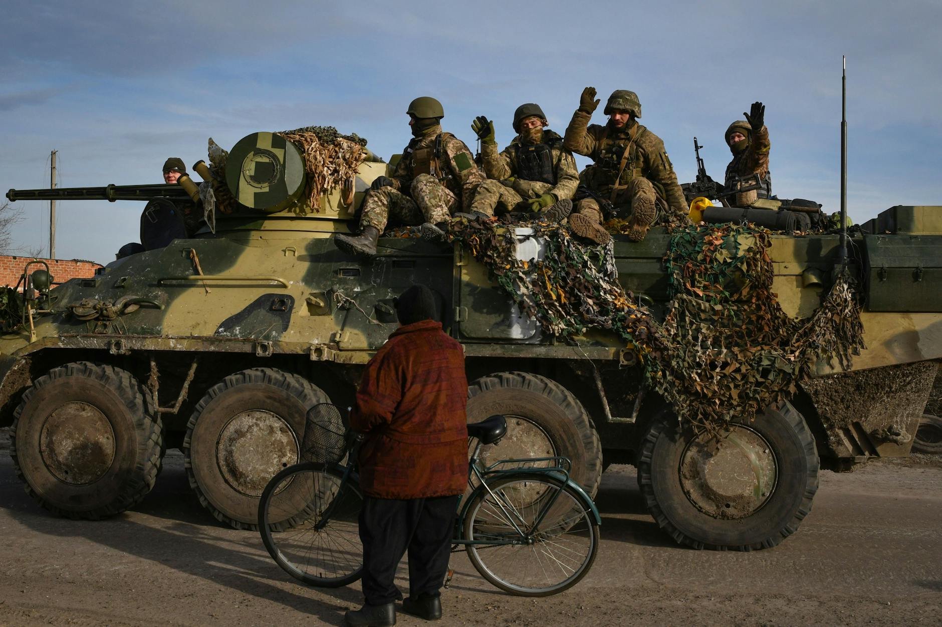 Ukrainische Soldaten winken einem Anwohner zu, während sie auf einem Militärfahrzeug vorbeifahren. 