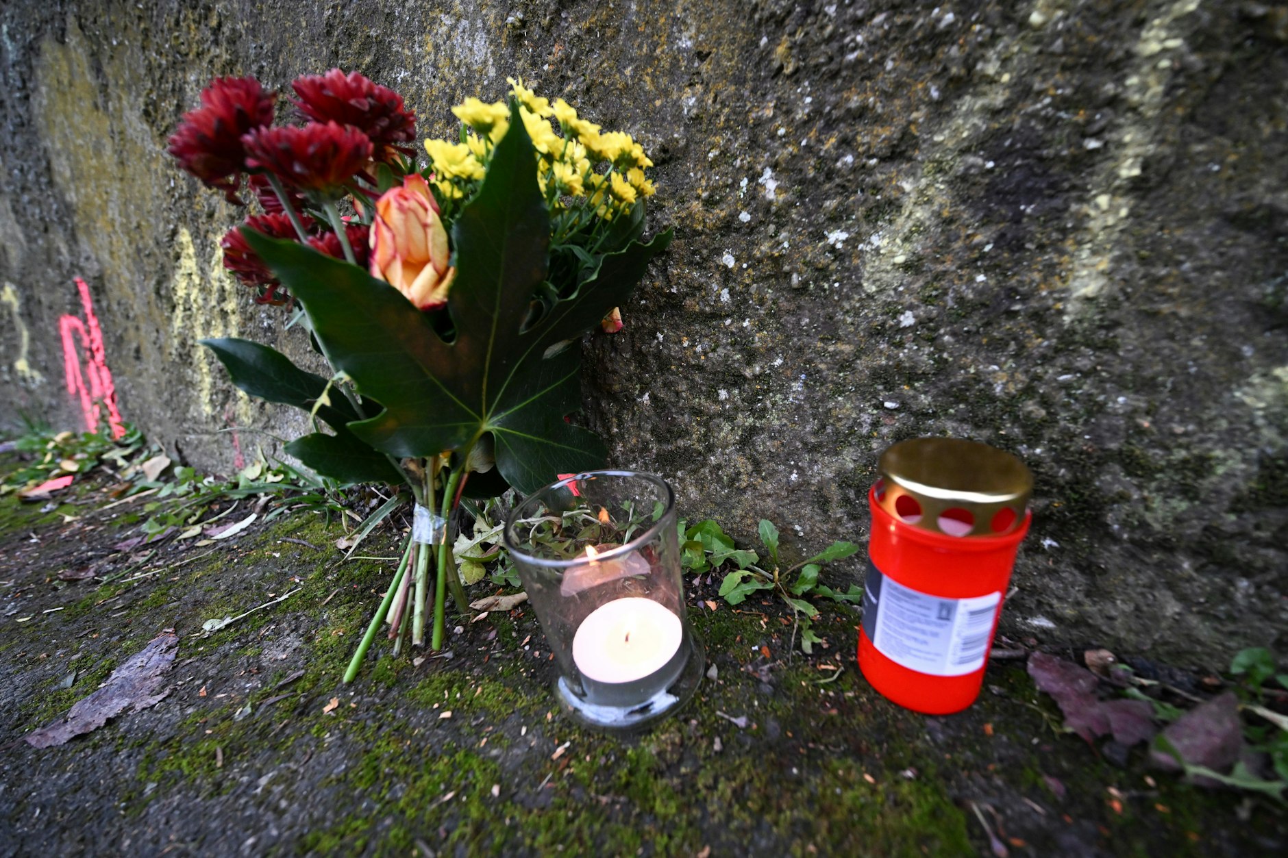 Am Tator5t haben Bewohner Blumen und Kerzen gestellt. Dahinter sind die Markierungen der Spurensicherung der Polizei zu sehen.
