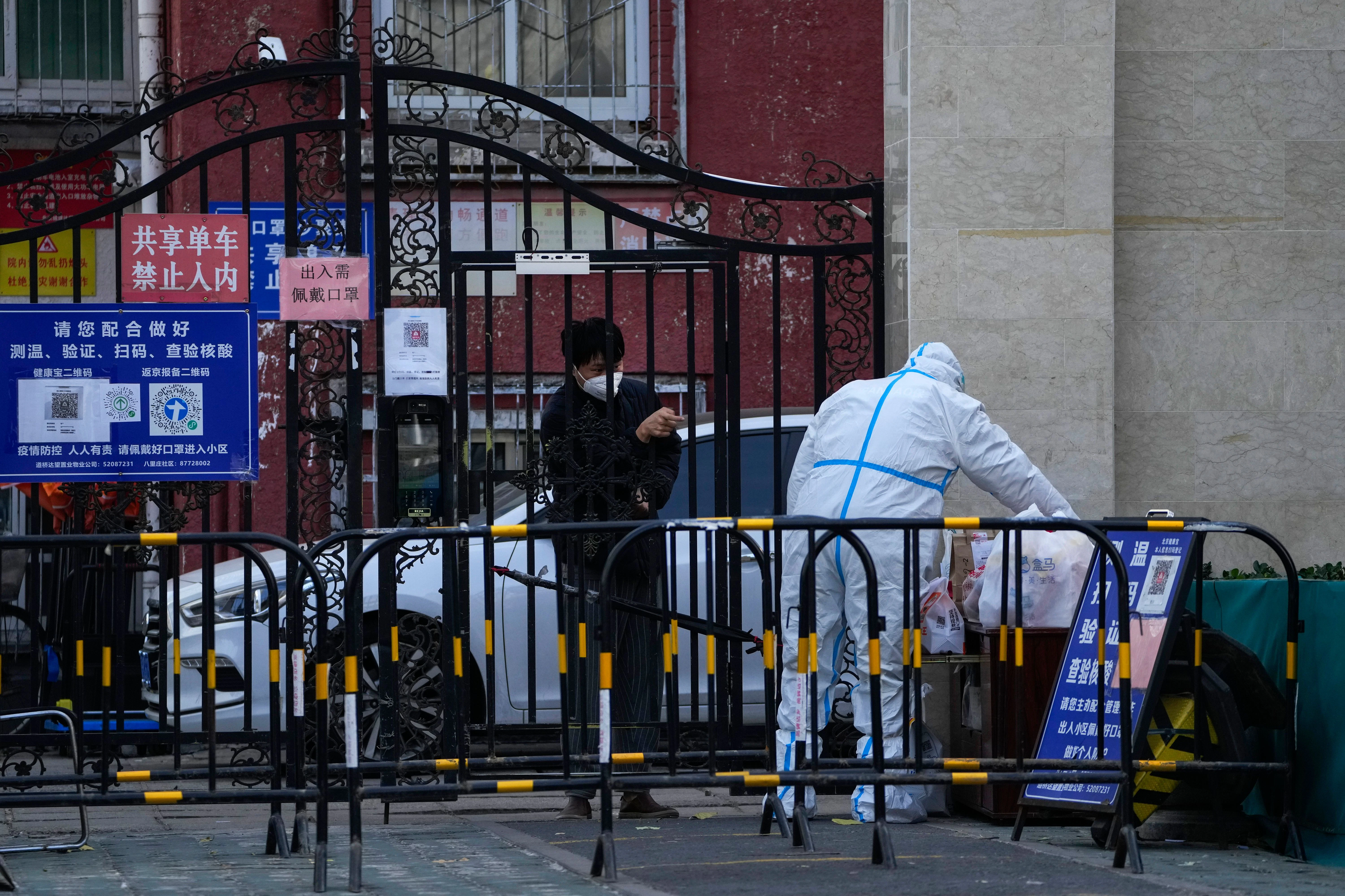 Ein Mann bittet einen Arbeiter mit Schutzanzug, seine Lebensmittel in einem abgesperrten Viertel in Peking abzuholen.