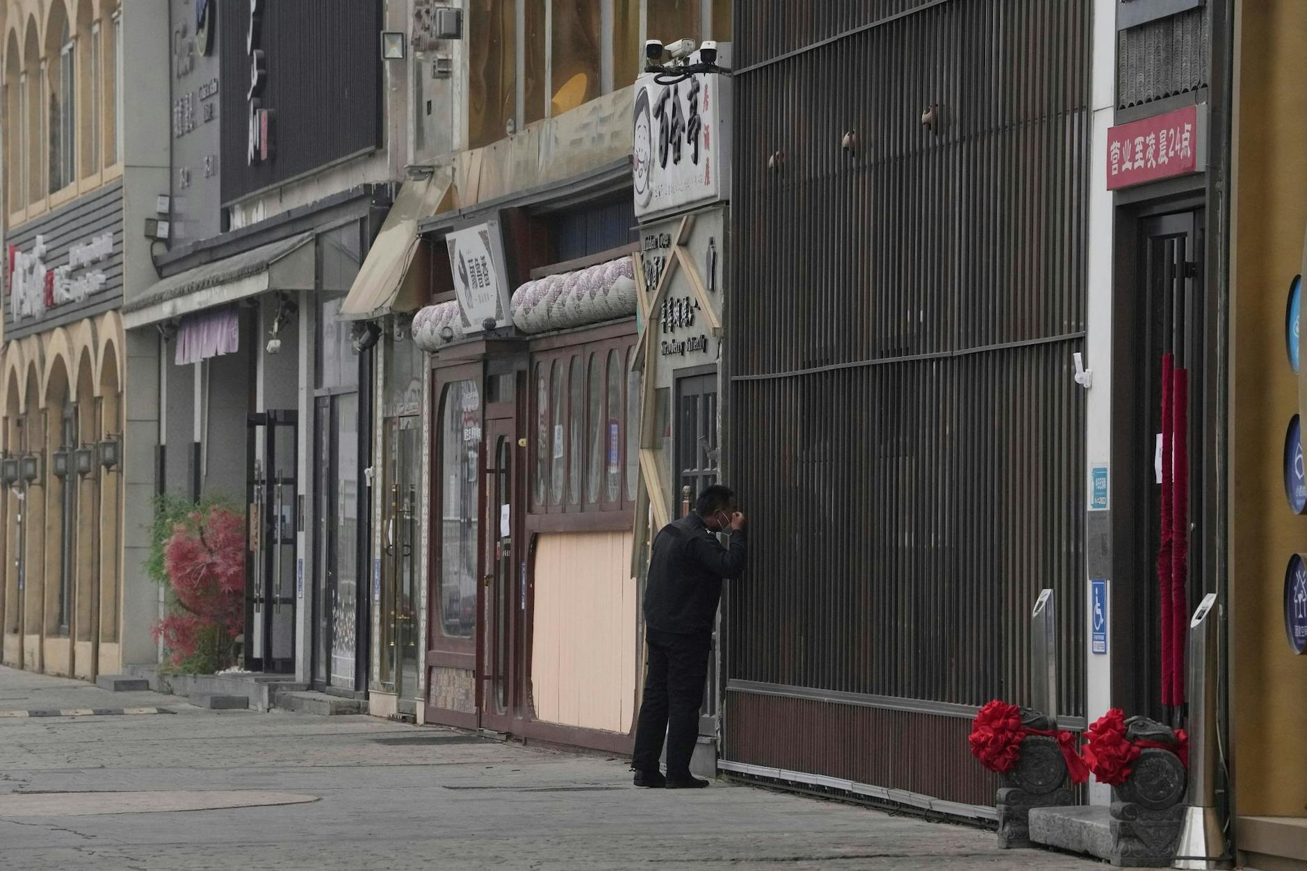 Ein Sicherheitsbeamter blickt in ein Geschäft entlang einer Reihe von geschlossenen Restaurants in Peking. Eine Rekord-Welle neuer Corona-Infektionen führt in China zu immer größeren Einschränkungen für die Bevölkerung.