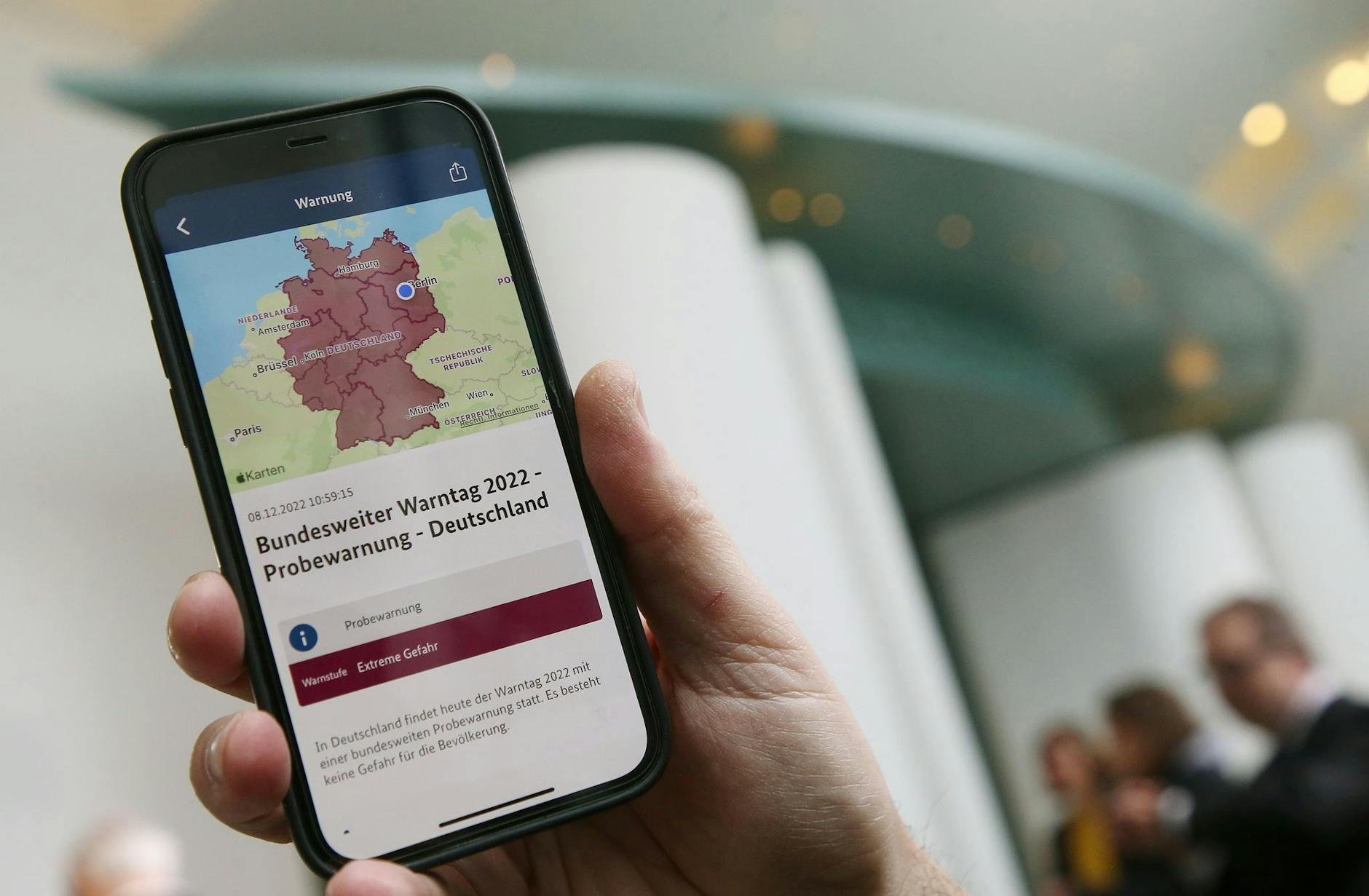 Ein Mitarbeiter des Bundeskanzleramts hält sein Mobiltelefon am Warntag 2022 im Foyer des Kanzleramtes in der Hand.