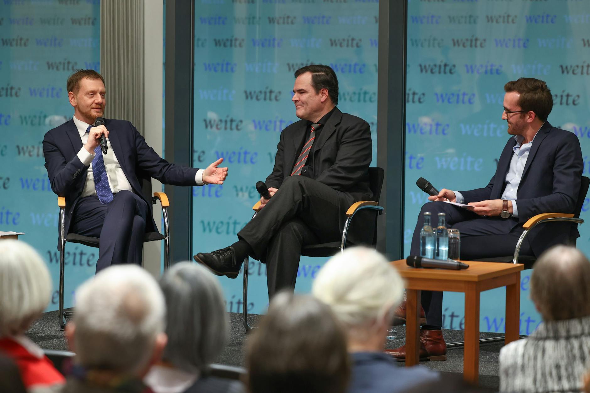 8.12.2022, Berlin: Sachsens Ministerpräsident Michael Kretschmer (CDU), Autor Uwe Tellkamp und Journalist Martin Machowecz (v.l.n.r.) sitzen bei einer Lesung in der Landesvertretung Sachsens auf der Bühne.