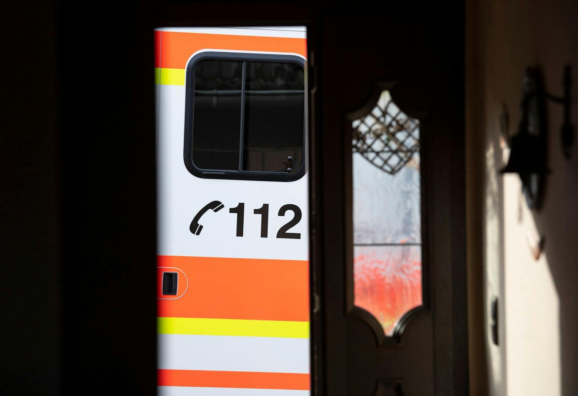 ARCHIV - Ein Rettungswagen parkt vor der geöffneten Tür eines Wohnhauses.  