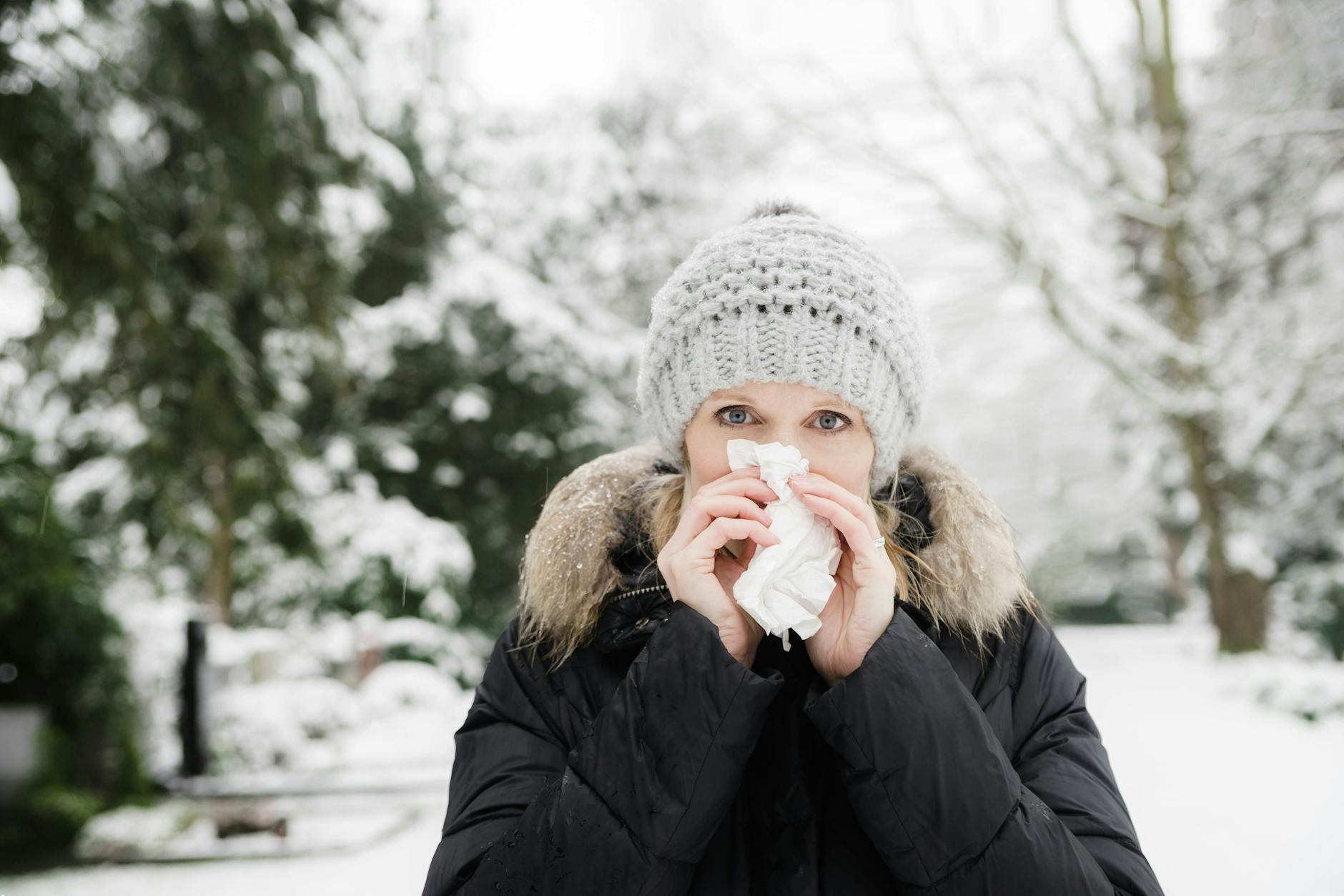 Eine Frau putzt sich draußen im Winter die Nase.