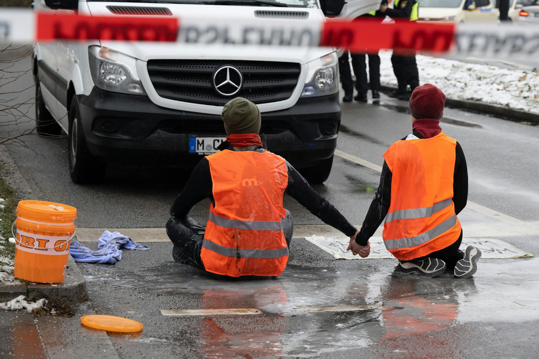 Mitglieder der Gruppe „Letzte Generation“ versuchen, sich auf einer Straße trotz Nieselregen und Minusgraden festzukleben. 