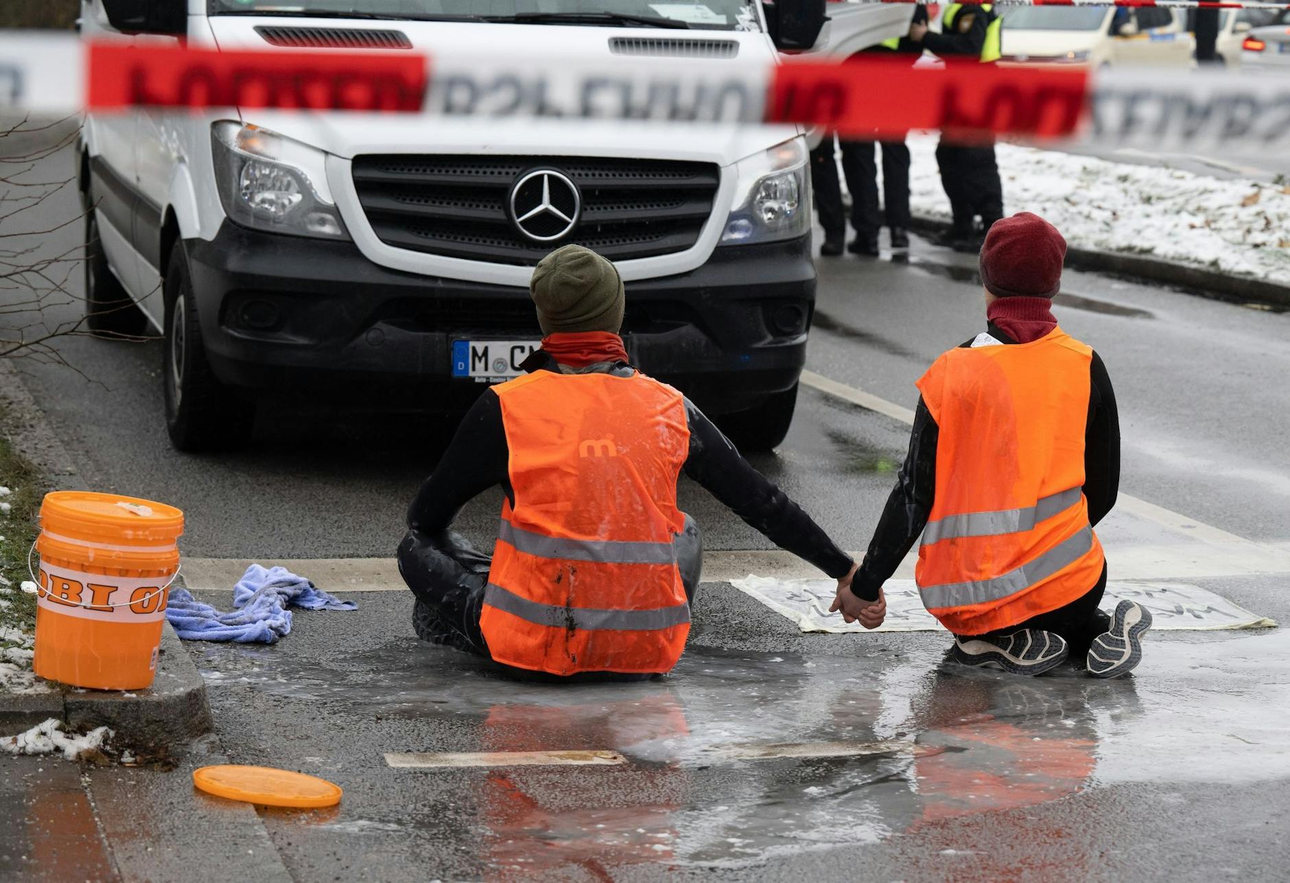 dpatopbilder - Zwei Klimaaktivisten der «Letzten Generation» versuchen, sich auf einer Straße in München trotz Nieselregen und Minusgraden festzukleben.