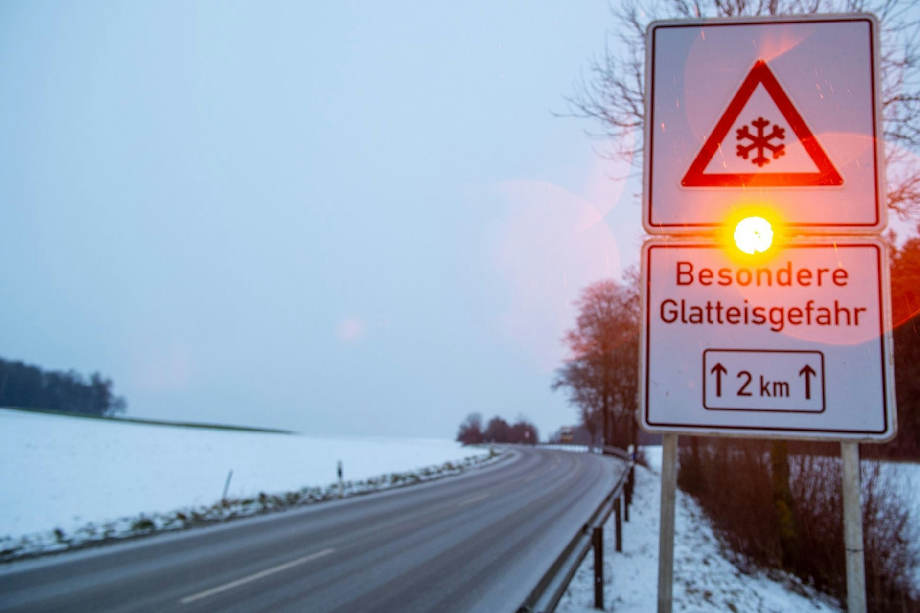 Ein Straßenschild warnt mit einer Blinkleuchte vor Glatteis. 