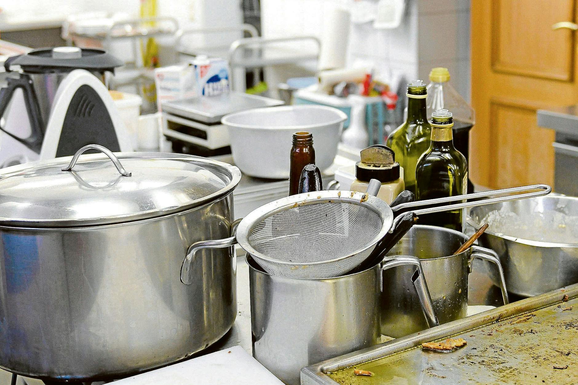 Töpfe, Siebe, Pfannen türmen sich auf einem Herd in einer Restaurantküche.