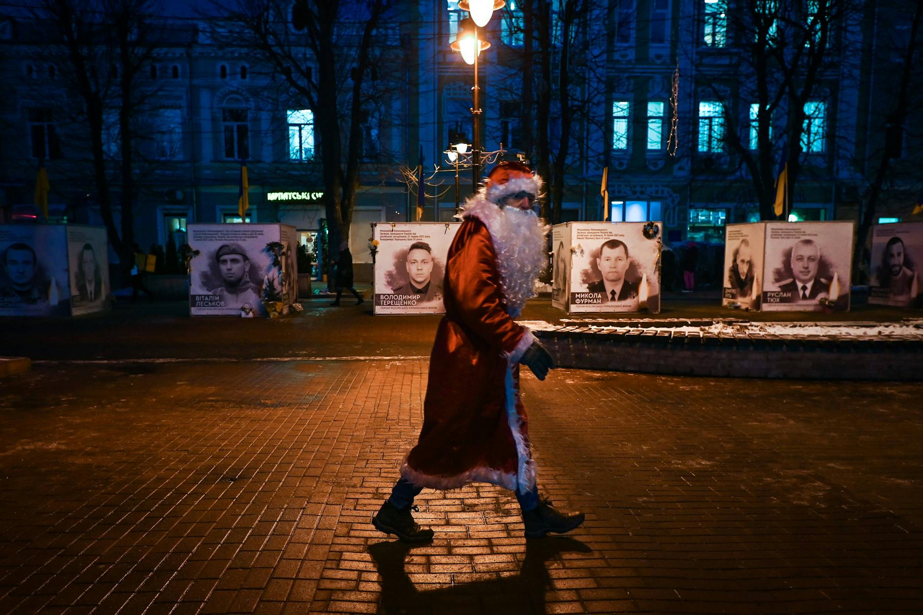 In der ukrainischen Stadt Khmelnytskyi läuft ein Weihnachtsmann. Im Hintergrund eine Bilder-Ausstellung getöteter Ukrainer.