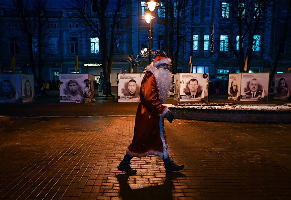 In der ukrainischen Stadt Khmelnytskyi läuft ein Weihnachtsmann. Im Hintergrund eine Bilder-Ausstellung getöteter Ukrainer.