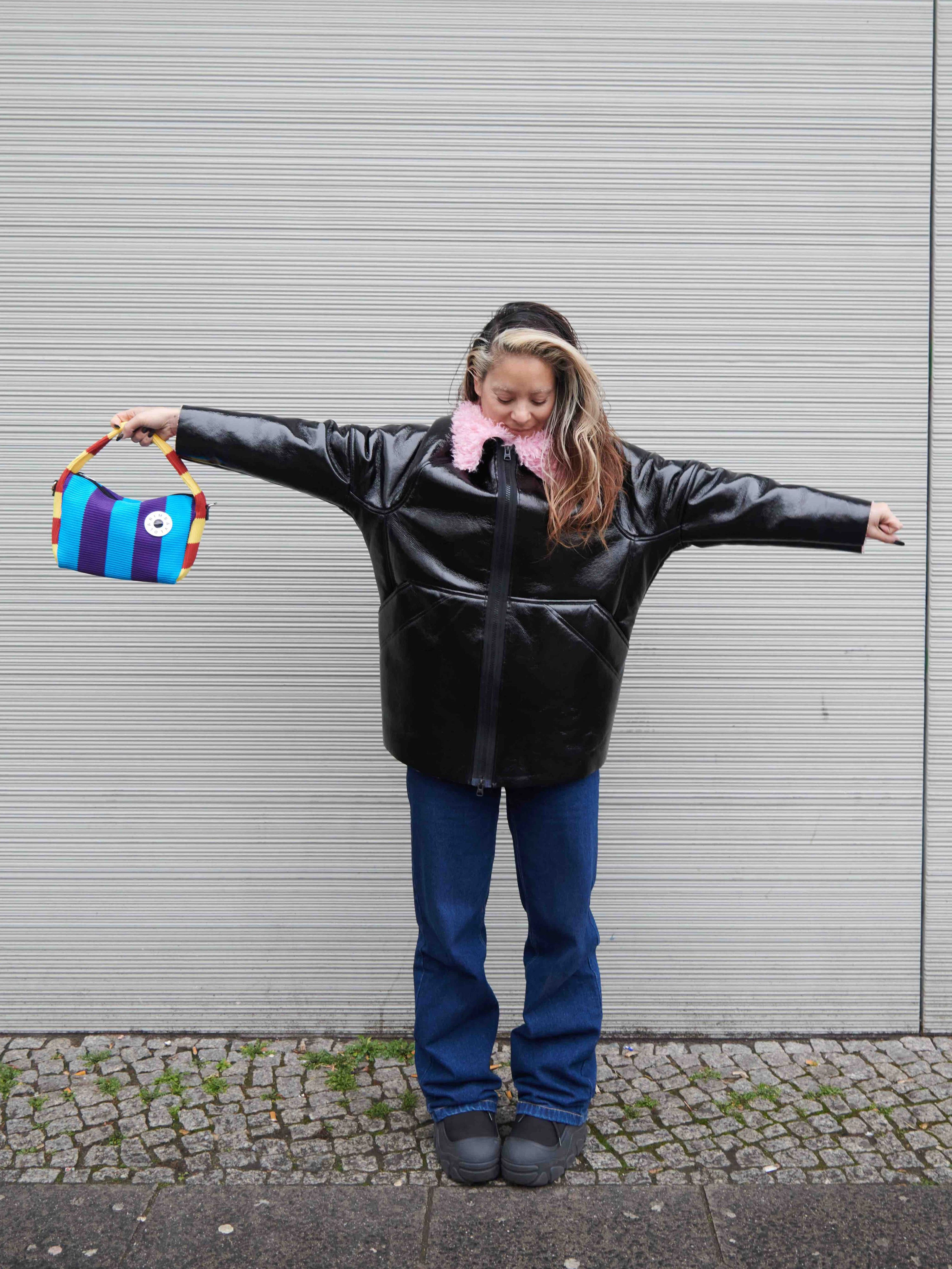 Mika ist Unternehmerin. Als Inhaberin der PR-Agentur Moriyama Projects mit Sitz im Aufbau Haus betreut sie vor allem Kunden aus der Fashionbranche. Sie trägt eine vegane Lacklederjacke mit rosa Plüschfutter von Bimba Y Lola und eine Bootcut-Jeans von Karl Kani.&nbsp;