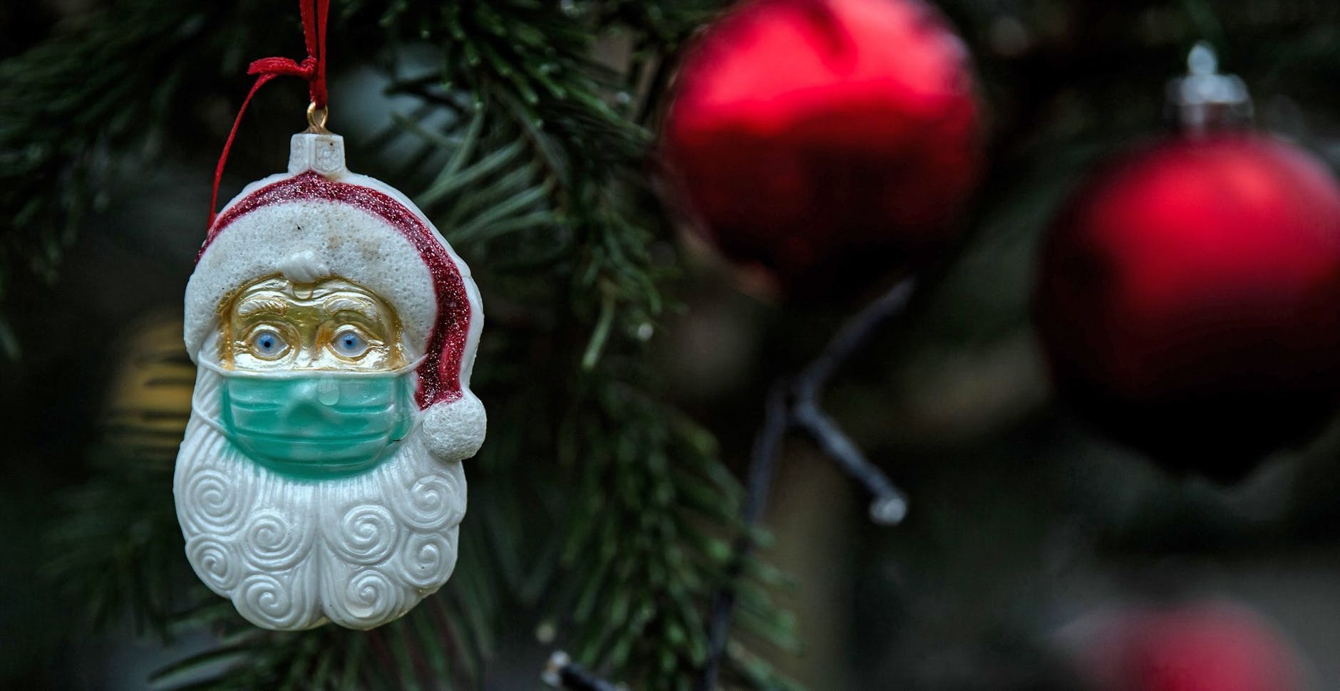 ARCHIV - Ein Weihnachtsmann mit einer Schutzmaske hängt als Weihnachtsbaumschmuck in einem Tannenbaum.
