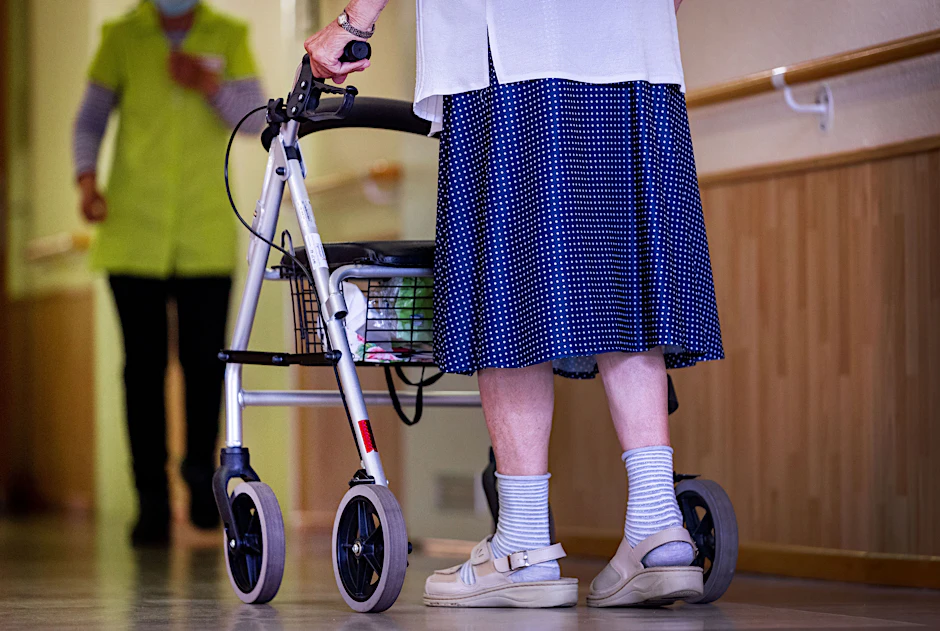 Eine ältere Dame geht mit ihrem Rollator über den Flur eines Pflegeheims.