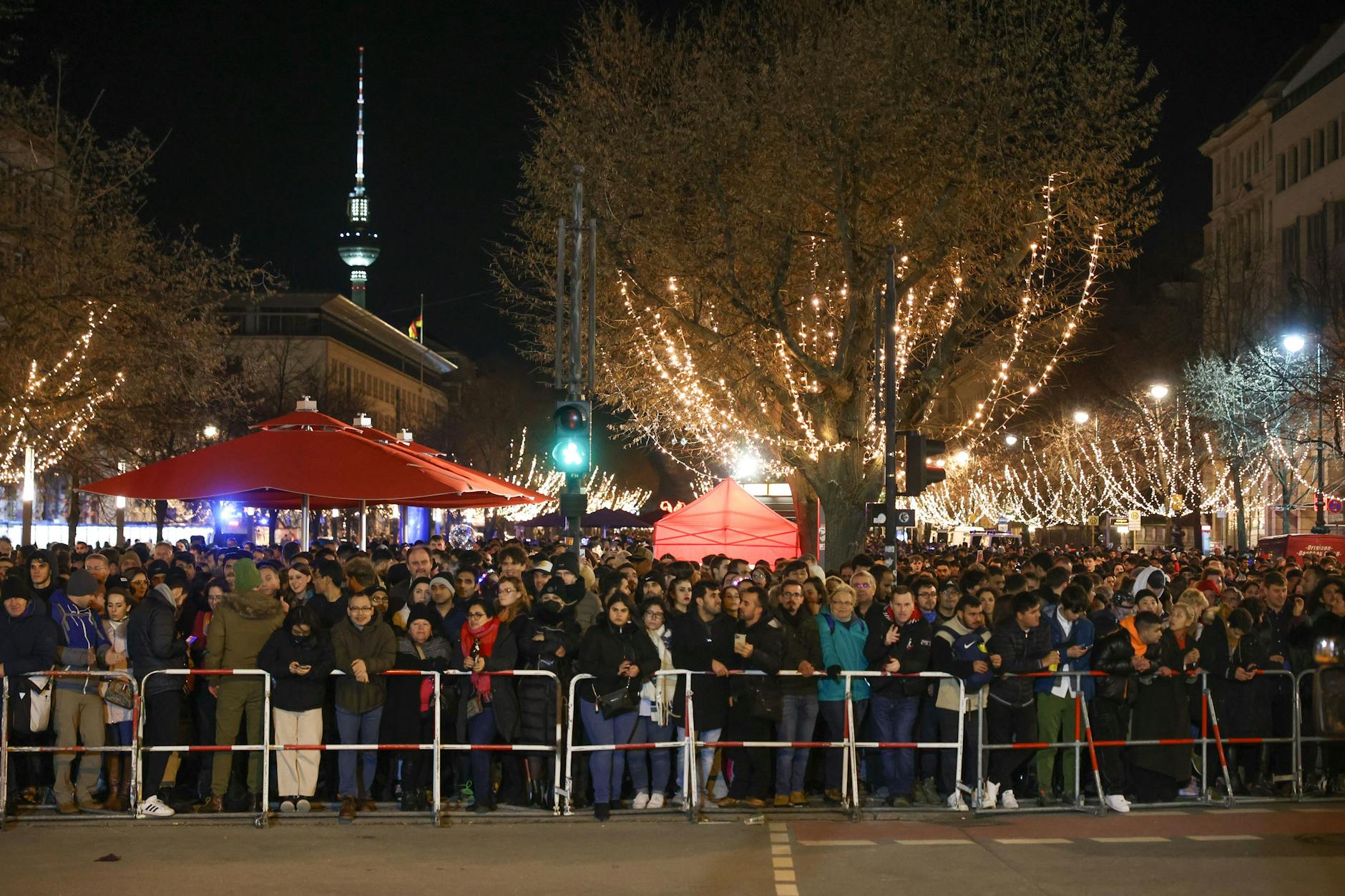 Zahlreiche Menschen stehen am Silvesterabend hinter einer Absperrung an der Straße Unter den Linden. Sie verfolgen eine TV-Show des ZDF, die live vom Brandenburger Tor ausgestrahlt wird. 