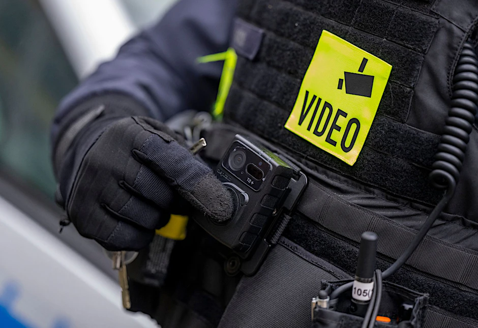 Ein Polizist schaltet die Bodycam auf seiner Uniform ein.