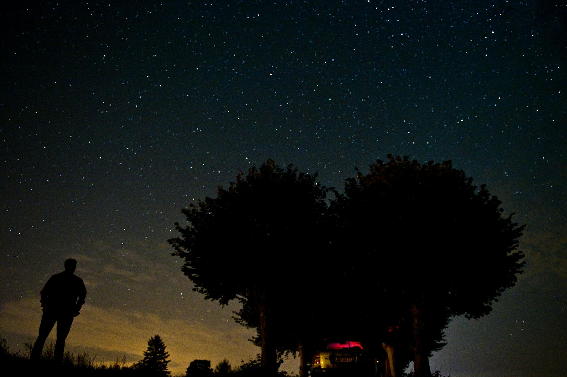 Ein Mann steht auf einem Feld und schaut in den Sternenhimmel.