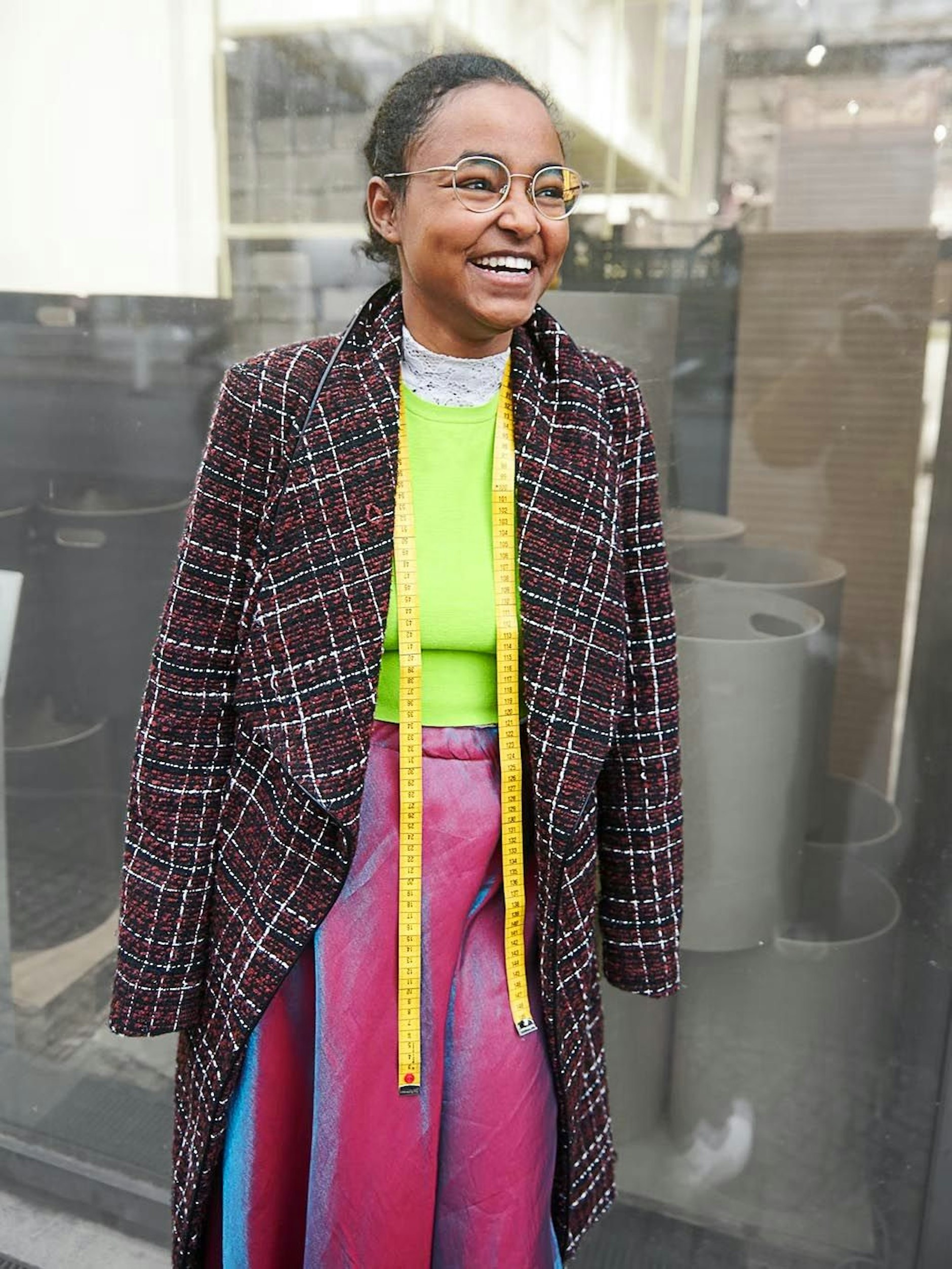 Ayenachew hat im Alter von sechs Jahren angefangen zu nähen. Aus dem rotblau schimmernden Jugendweihekleid ihrer Mutter hat sie sich einen Rock genäht. Auch das neongrüne Top mit Spitzenkragen besteht aus geänderten Kleidungsstücken ihrer Mutter. Ayenachew liebt Kleidungsstücke, die bereits eine Geschichte haben, erzählt sie.