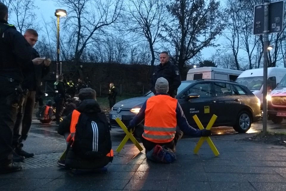 Mitglieder der Letzten Generation sitzen mit gelben Kreuzen am Tempelhofer Damm. 