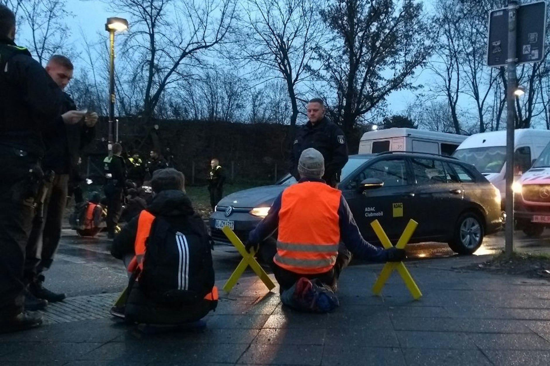 Mitglieder der Letzten Generation sitzen mit gelben Kreuzen am Tempelhofer Damm. 