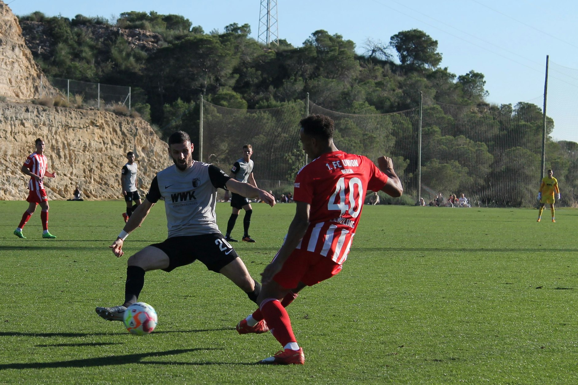 Jamie Leweling (r.) spielt genau rechtzeitig ab, kurz bevor Augsburgs Routinier Daniel Caligiuri an den Ball kommen kann.