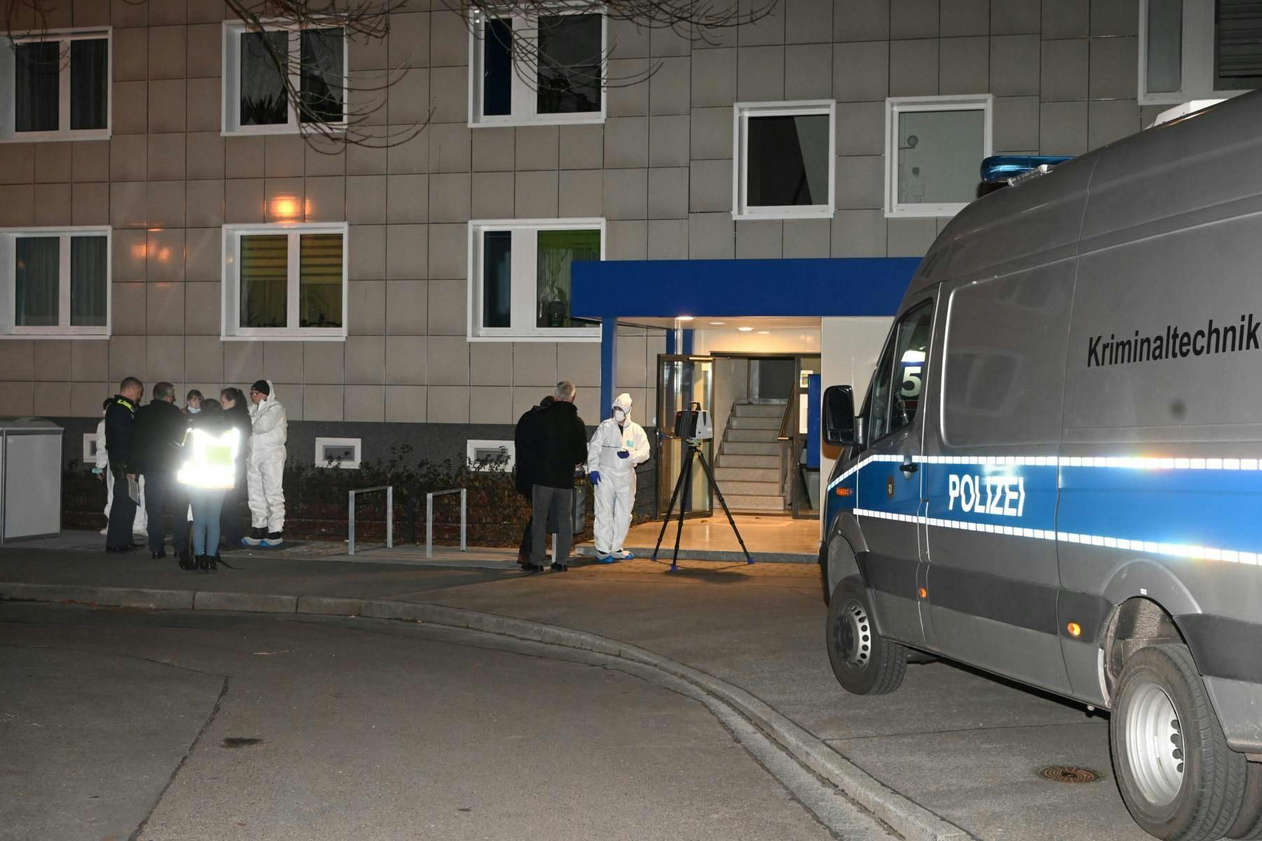 Kriminaltechniker in weißen Overalls stehen vor dem Hochhaus in Lichtenberg. 