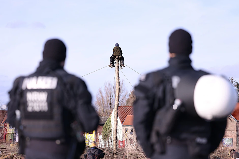 Polizisten beobachten zwei Klimaschutzaktivisten die auf einem Monopod am Rand des Braunkohledorfes Lützerath sitzen.  