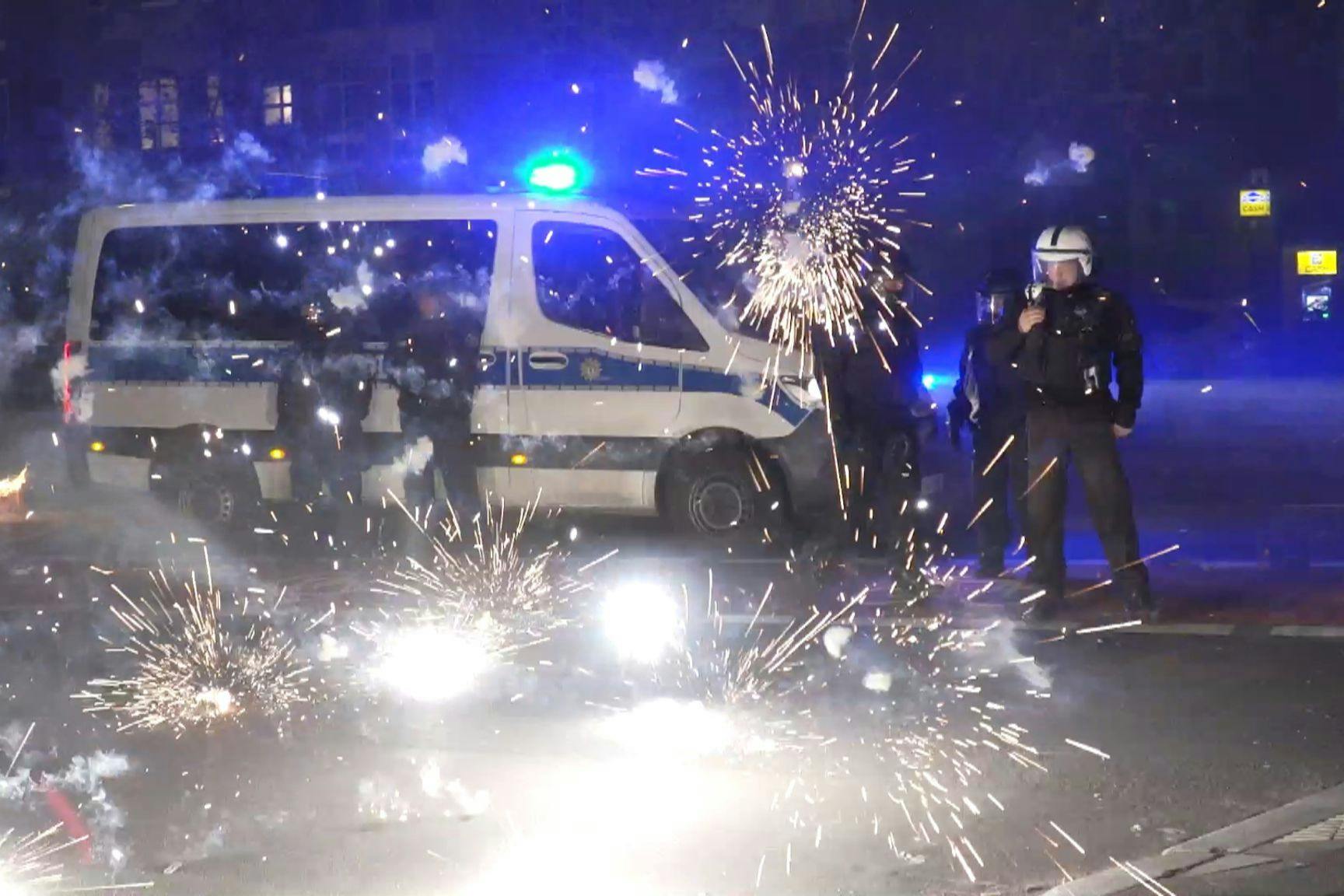 Berliner Polizisten stehen neben explodierendem Feuerwerk. 