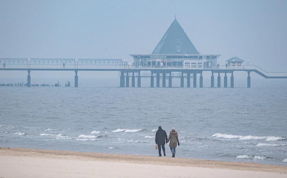 Ahlbeck: Spaziergänger sind am Strand der Insel Usedom unterwegs. In Zukunft soll der Urlaubsort mit dem Zug schneller von Berlin aus erreichbar sein.