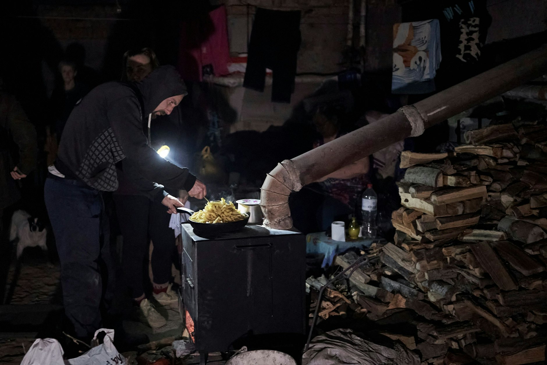 Ein Mann kocht auf einem Ofen in einem Keller in Soledar, ein Behelfs-Schlot führt nach außen: Das Leben der Zivilisten hat sich in Schutzräume verlagert. 
