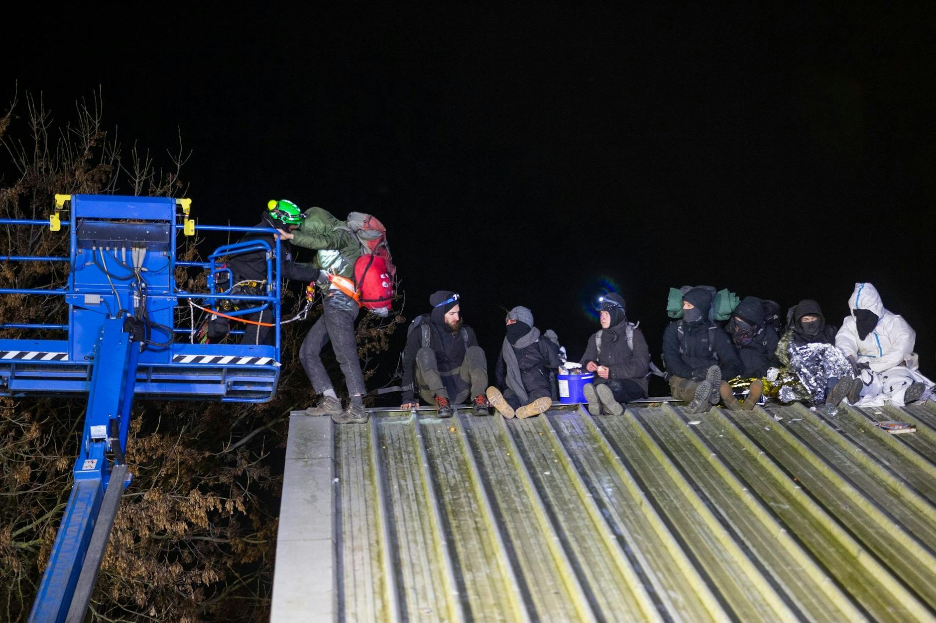 Klimaaktivisten sitzen auf einem Scheunendach und lassen sich von Höhenkletterer der Polizei herunterbringen.