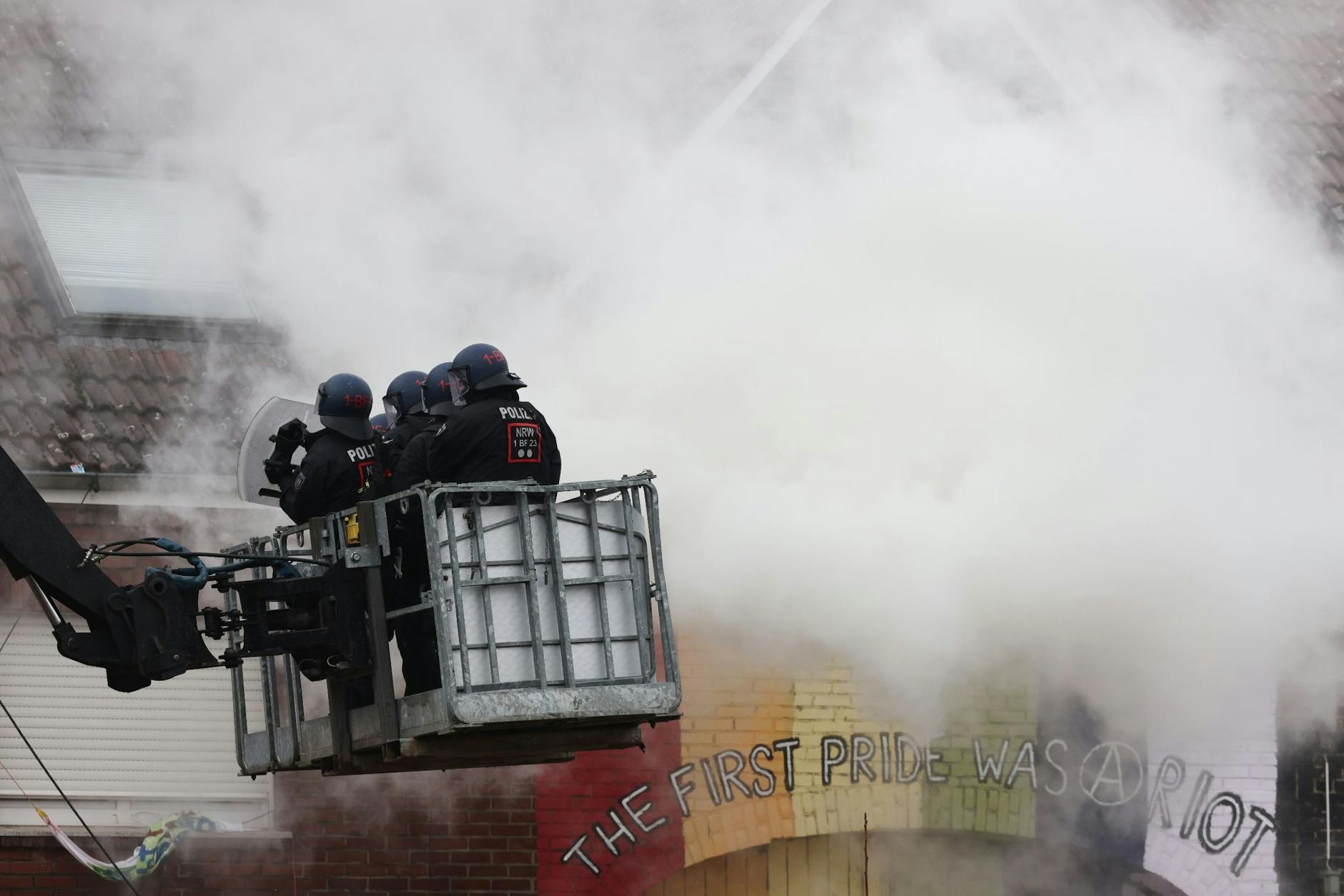 Polizisten stehen am zweiten Tag der Räumung im von Klimaaktivisten besetzten Braunkohleort Lützerath auf einer Hebebühne im Rauch von Pyrotechnik.