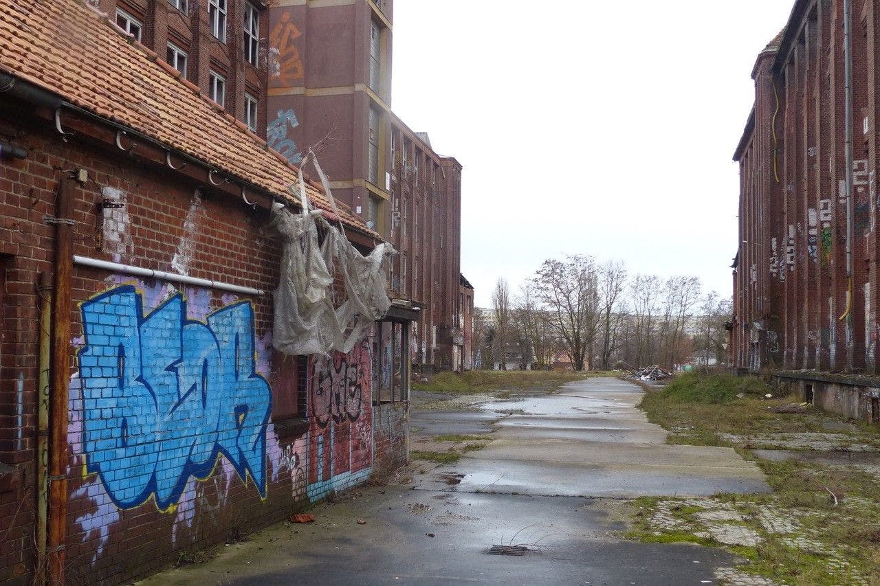 Die Zufahrt zum einstigen Kabelwerk von der Friedrichshagener Straße. Rechts und links die großen Fabrikationsgebäude, die wiederbelebt werden sollen. Im Hintergrund verläuft die Müggelspree.