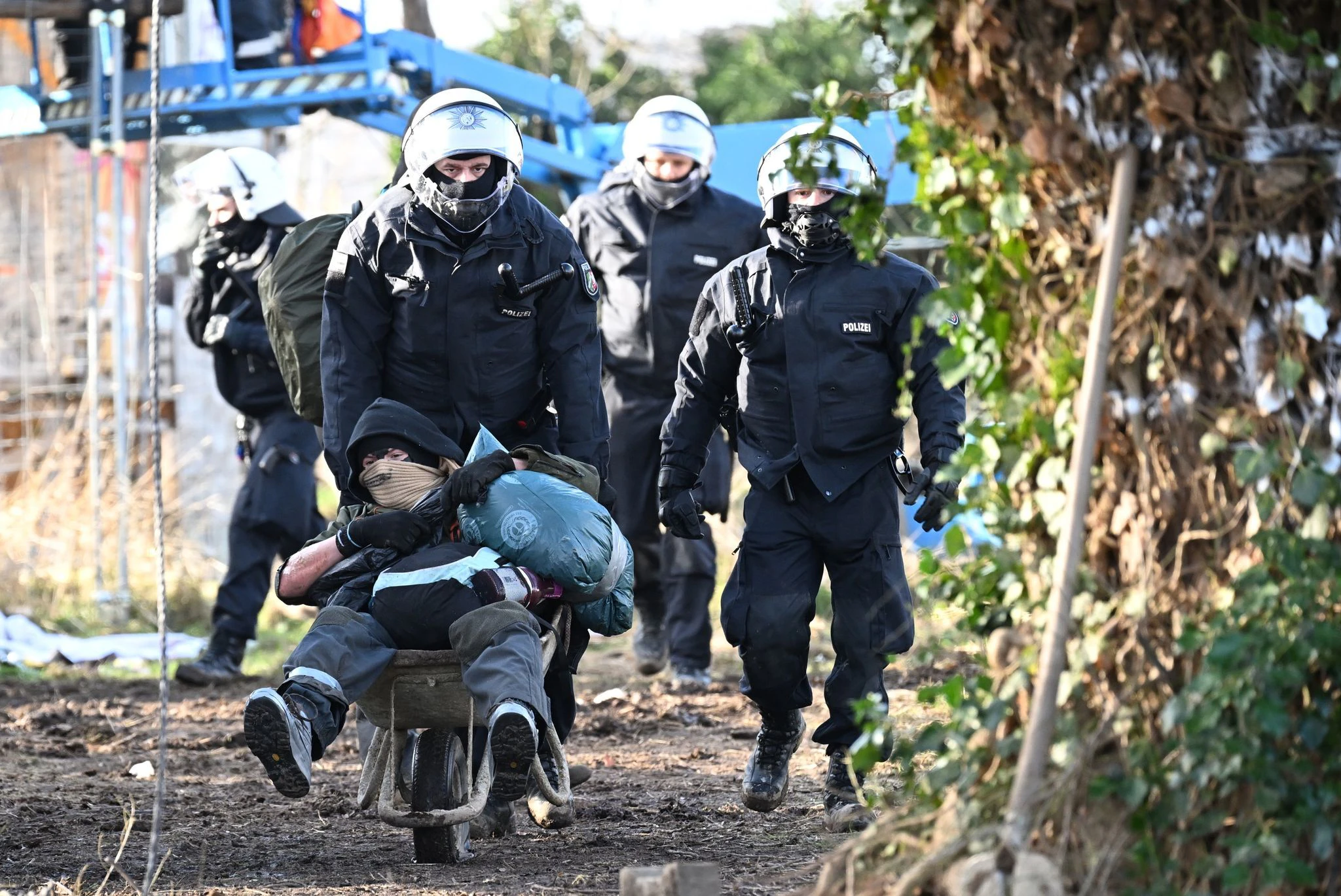 dpatopbilder - Polizisten schieben einen Klimaaktivisten mit einer Schubkarre aus Lützerath.  