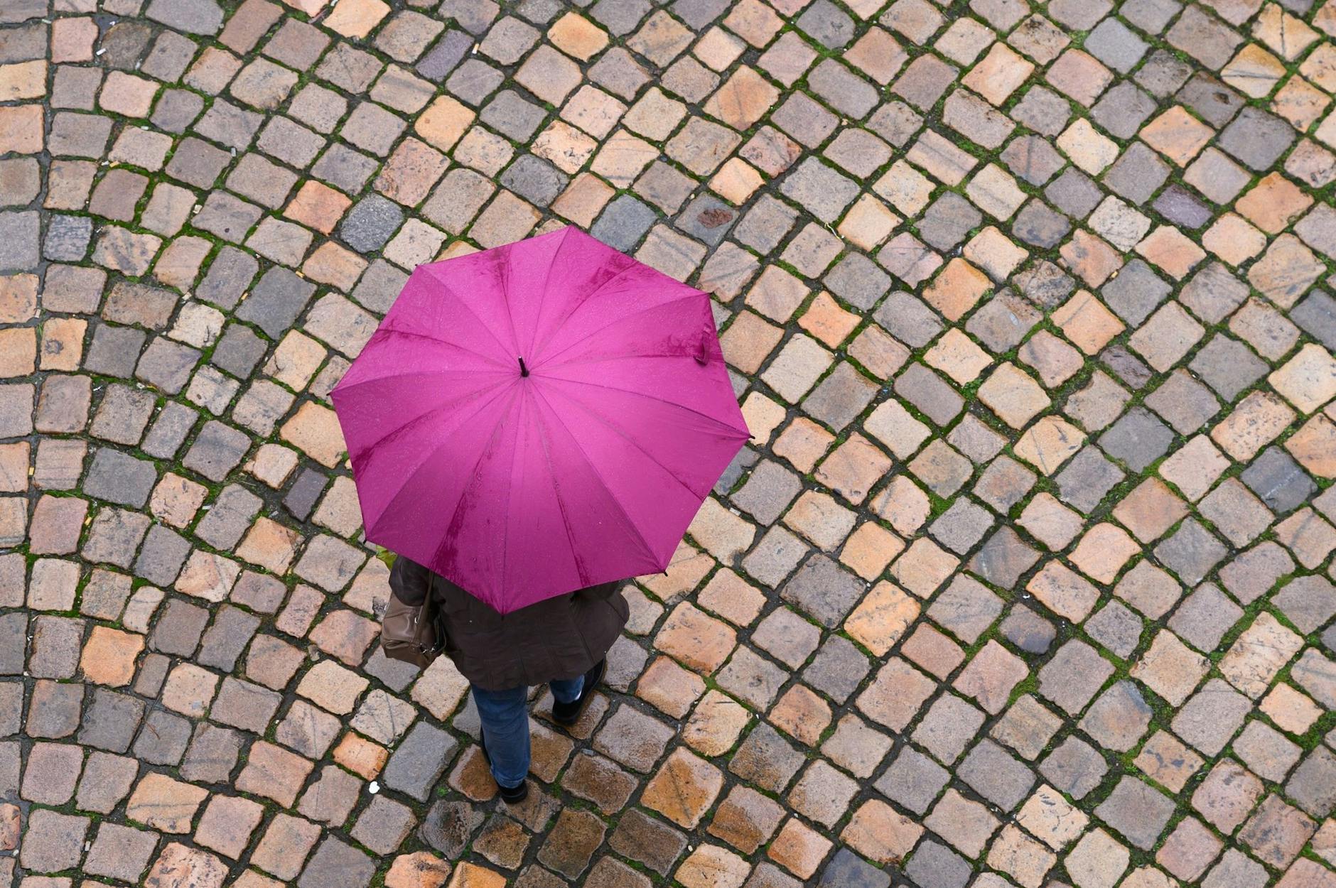 ARCHIV - Eine Frau geht mit einem Regenschirm auf einer Straße entlang. d/dpa/Symbolbild