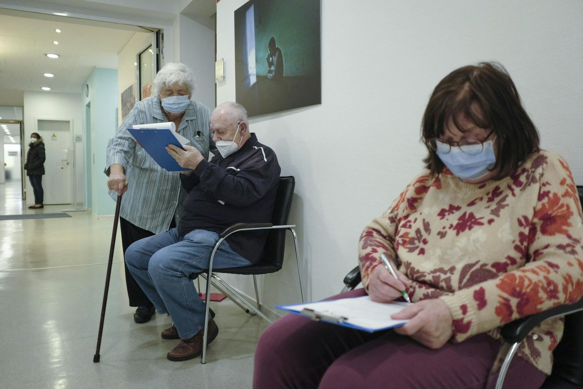 Patienten mit Schutzmasken im Flur einer Arztpraxis.