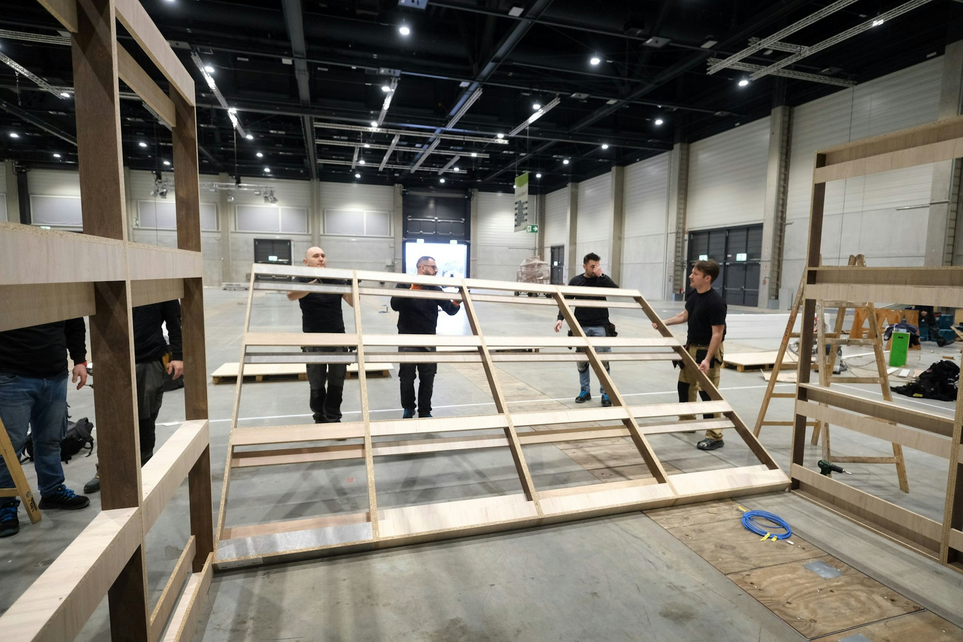 Aus Latten und Brettern bauen die Arbeiter aus Polen ein Gestell. Dann kommen außen schön aussehende Holzwände dran, fertig ist ein „Haus“ der temporären Messestadt.