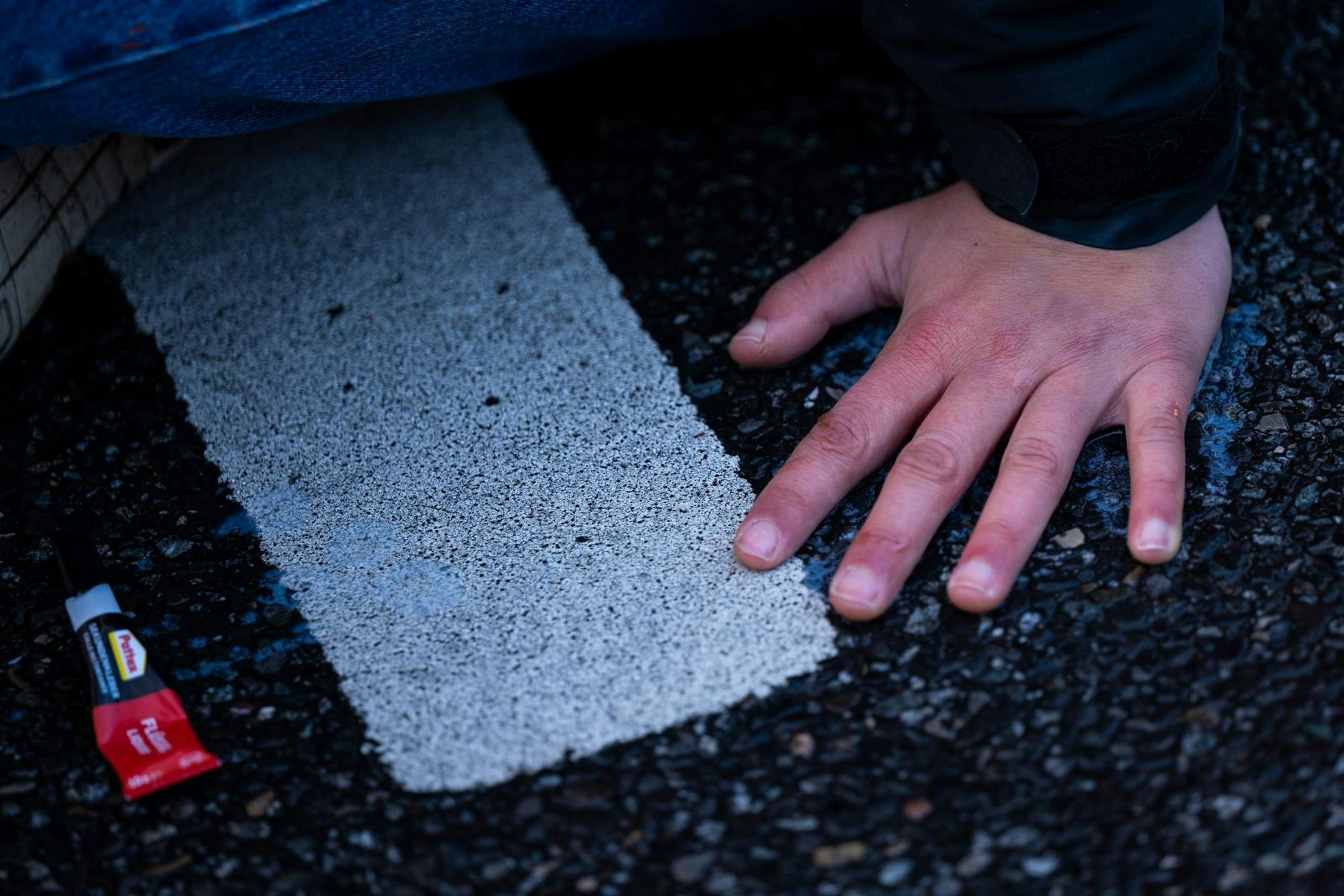 ARCHIV - Ein Klimaaktivist der Umweltschutzbewegung «Letzte Generation» klebt mit der Hand auf einer Straße.