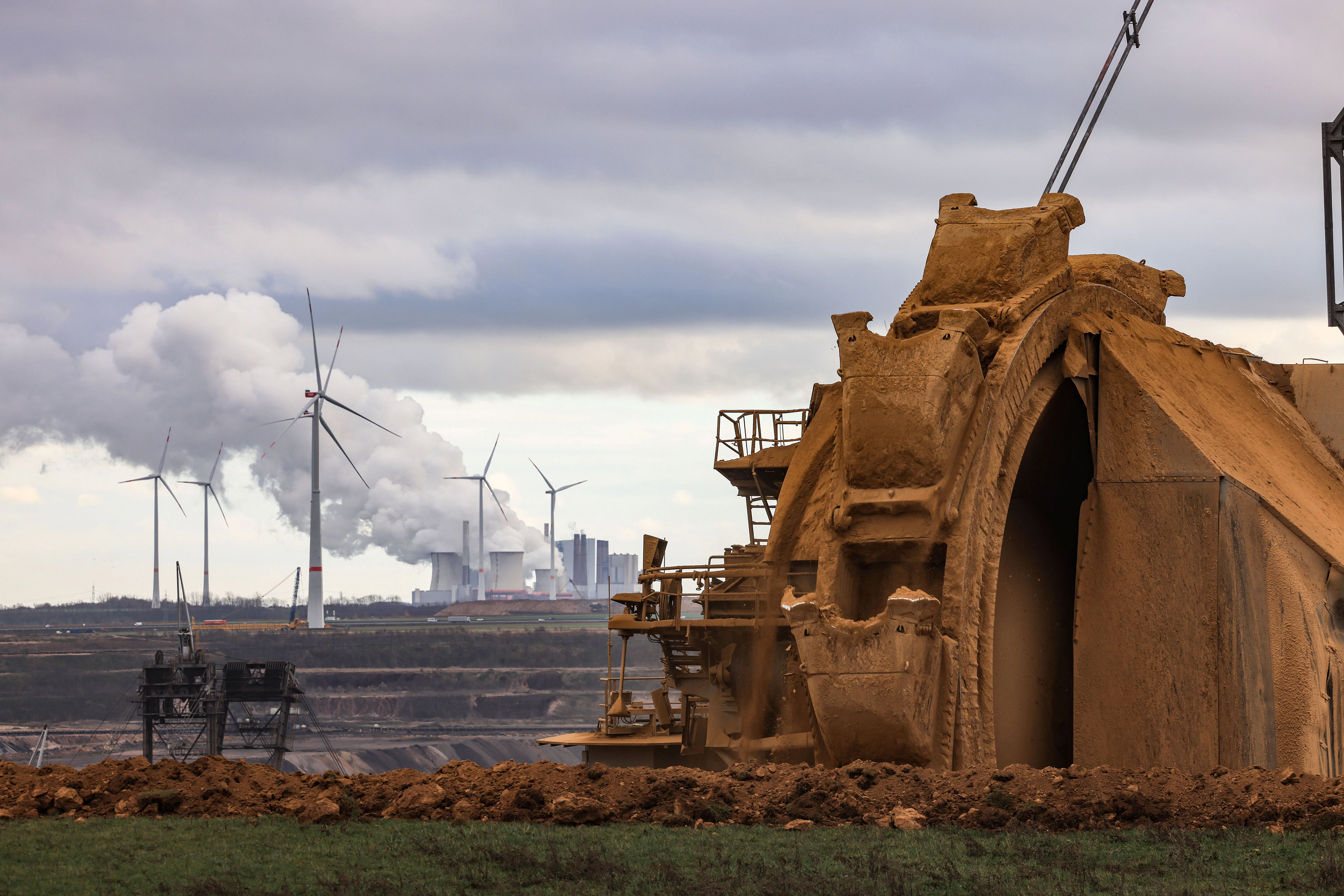 Ein Bagger schaufelt Erdreich am Rande des Braunkohletagebaus Garzweiler, im Hintergrund das Braunkohlekraftwerk Neurath.