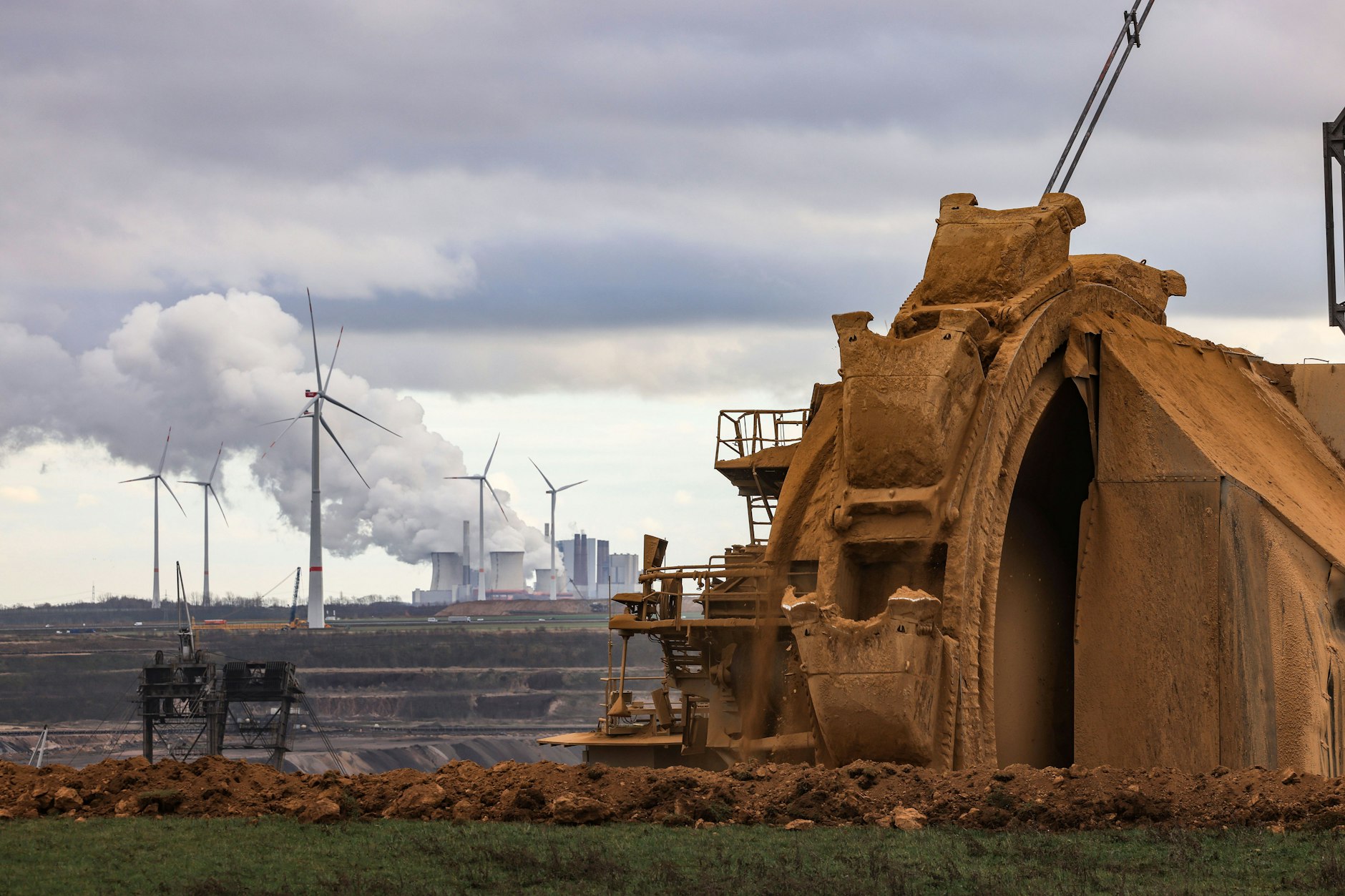 Ein Bagger schaufelt Erdreich am Rande des Braunkohletagebaus Garzweiler, im Hintergrund das Braunkohlekraftwerk Neurath.