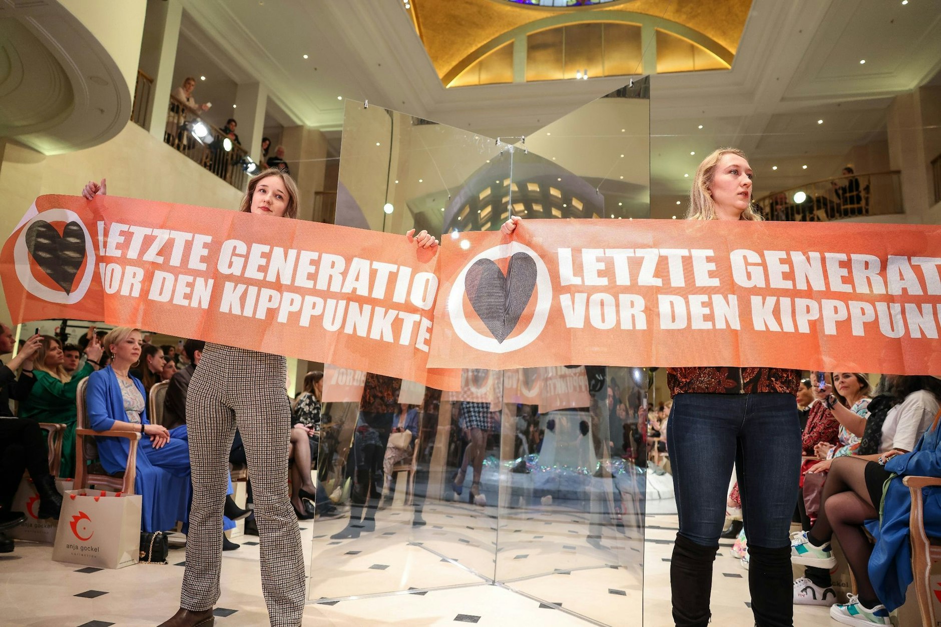 Demonstrantinnen der Gruppe Letzte Generation halten Transparente bei der Fashion Show der Designerin Anja Gockel.