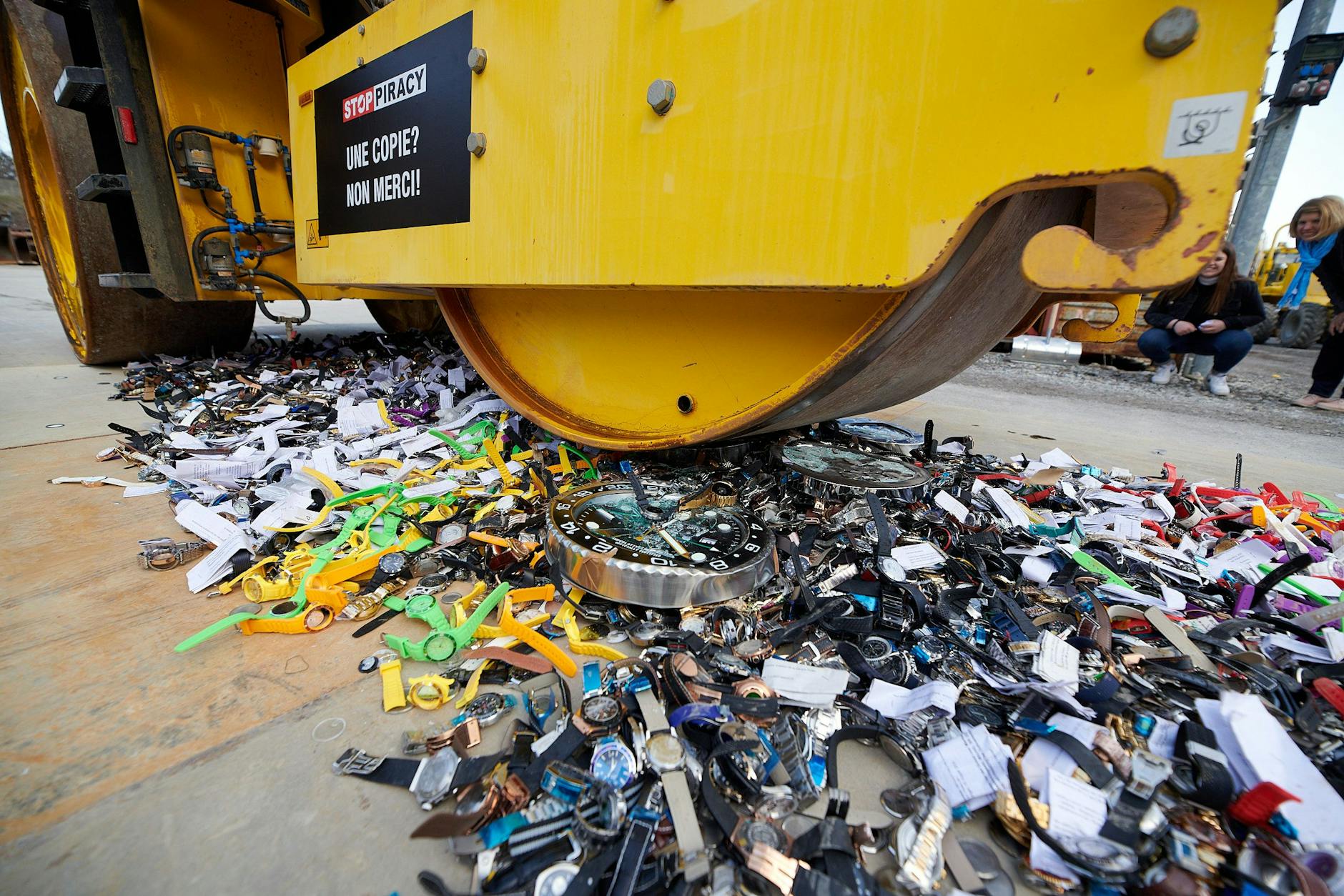 Kracks! Eine Straßenwalze zerstört nachgemachte Uhren. An der Seite der Maschine steht auf Französisch: Eine Kopie? Nein, danke!