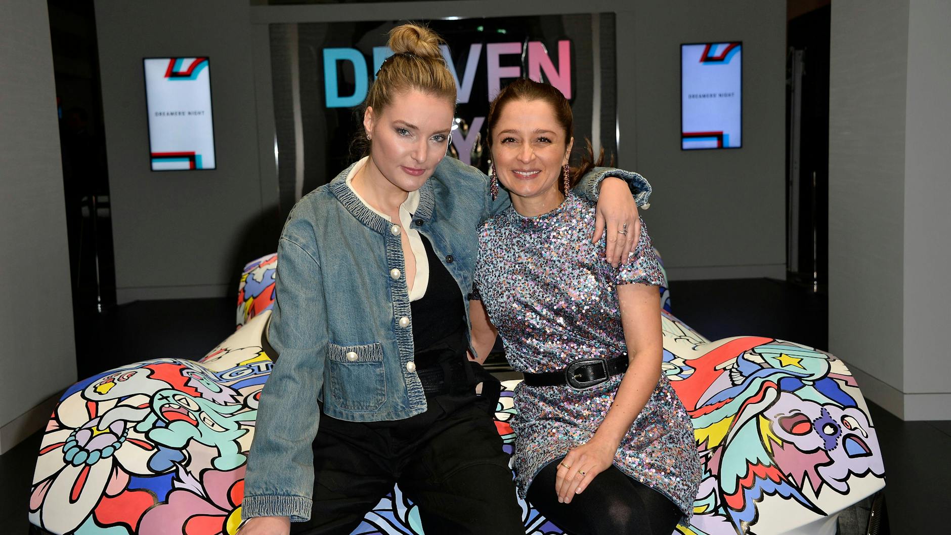 Influencerin Marie von den Benken und Schauspielerin Sarah Alles auf einem Graffiti-Boliden.