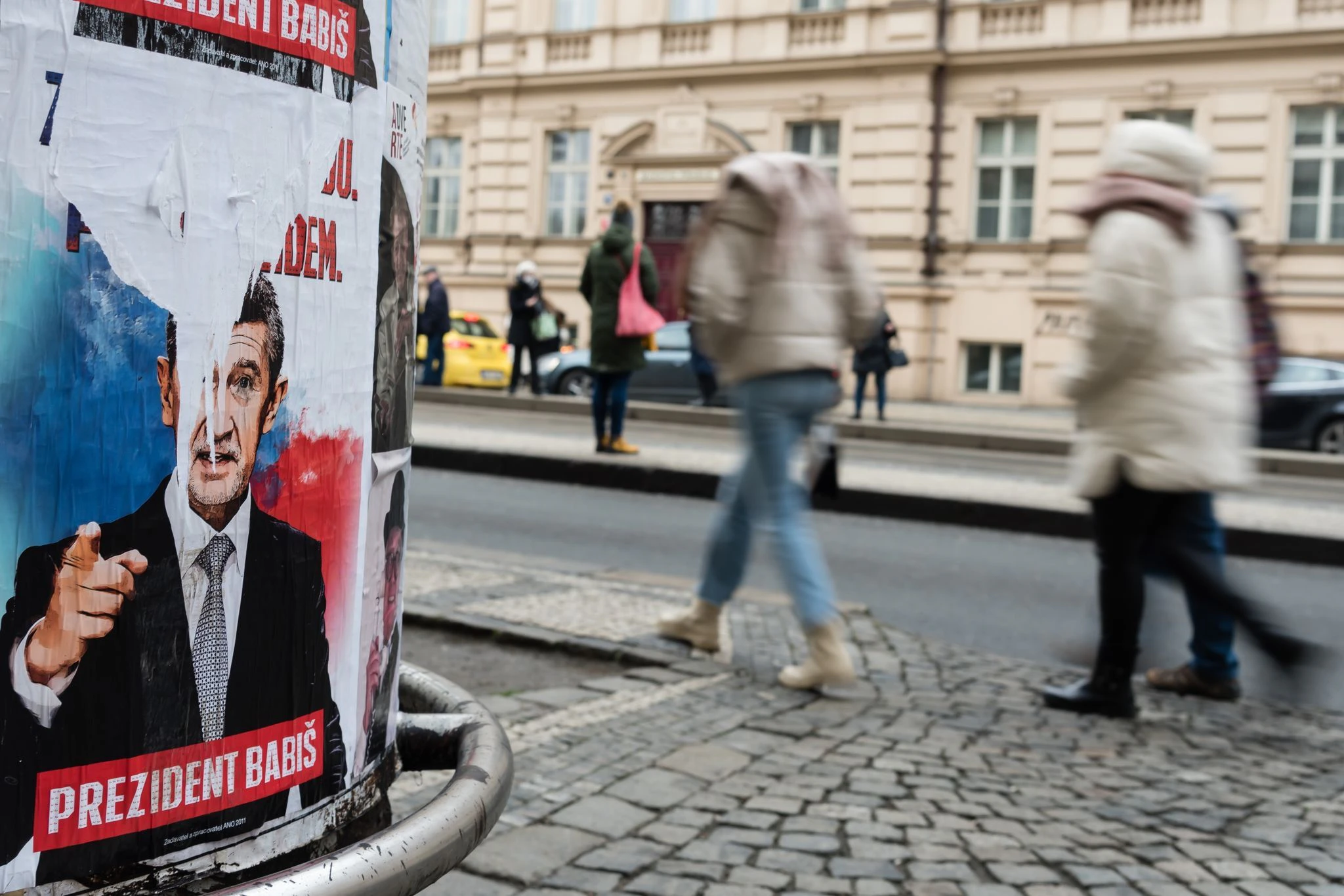 Menschen gehen an einem Wahlplakat für den Präsidentschaftskandidaten Andrej Babis vorbei, das auf einer Straße in Prag aufgestellt ist.  A Press Wire/dpa
