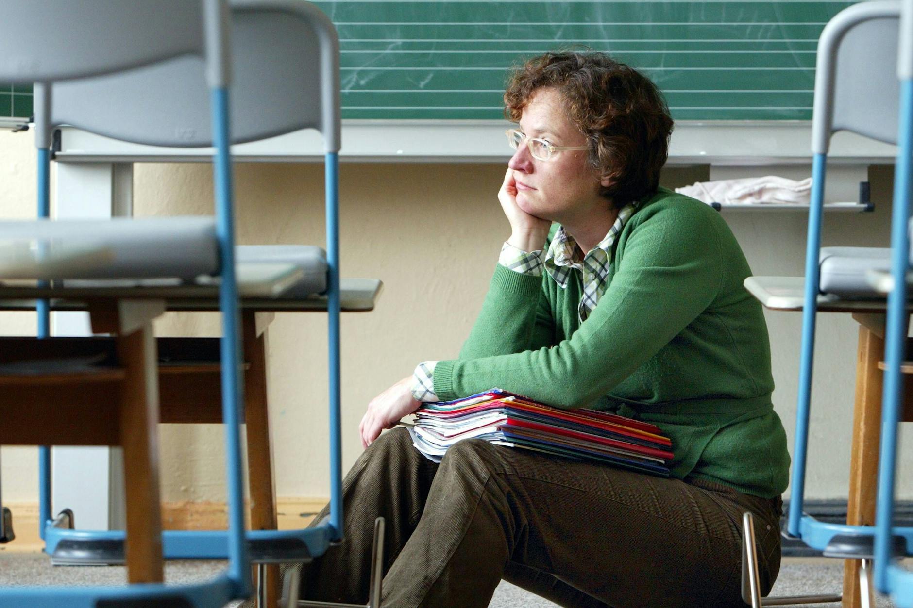 Eine Lehrerin sitzt alleine in einem Klassenraum. 
