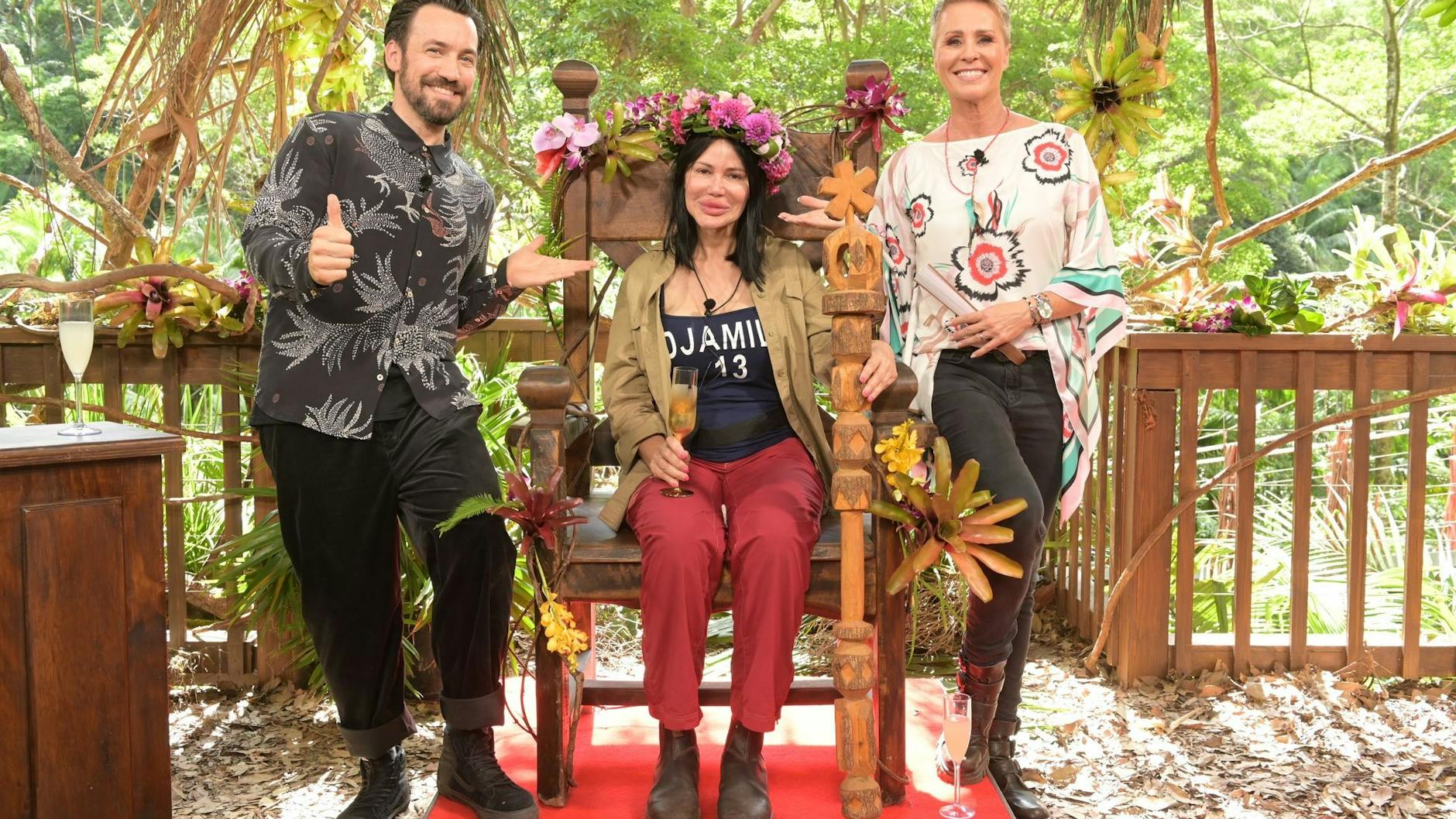 Djamila Rowe sitzt nach dem Sieg beim RTL-Dschungelcamp 2023 mit ihrer Krone auf ihrem Thron. Neben ihr stehen Moderatorin Sonja Zietlow und Moderator Jan Köppen.
